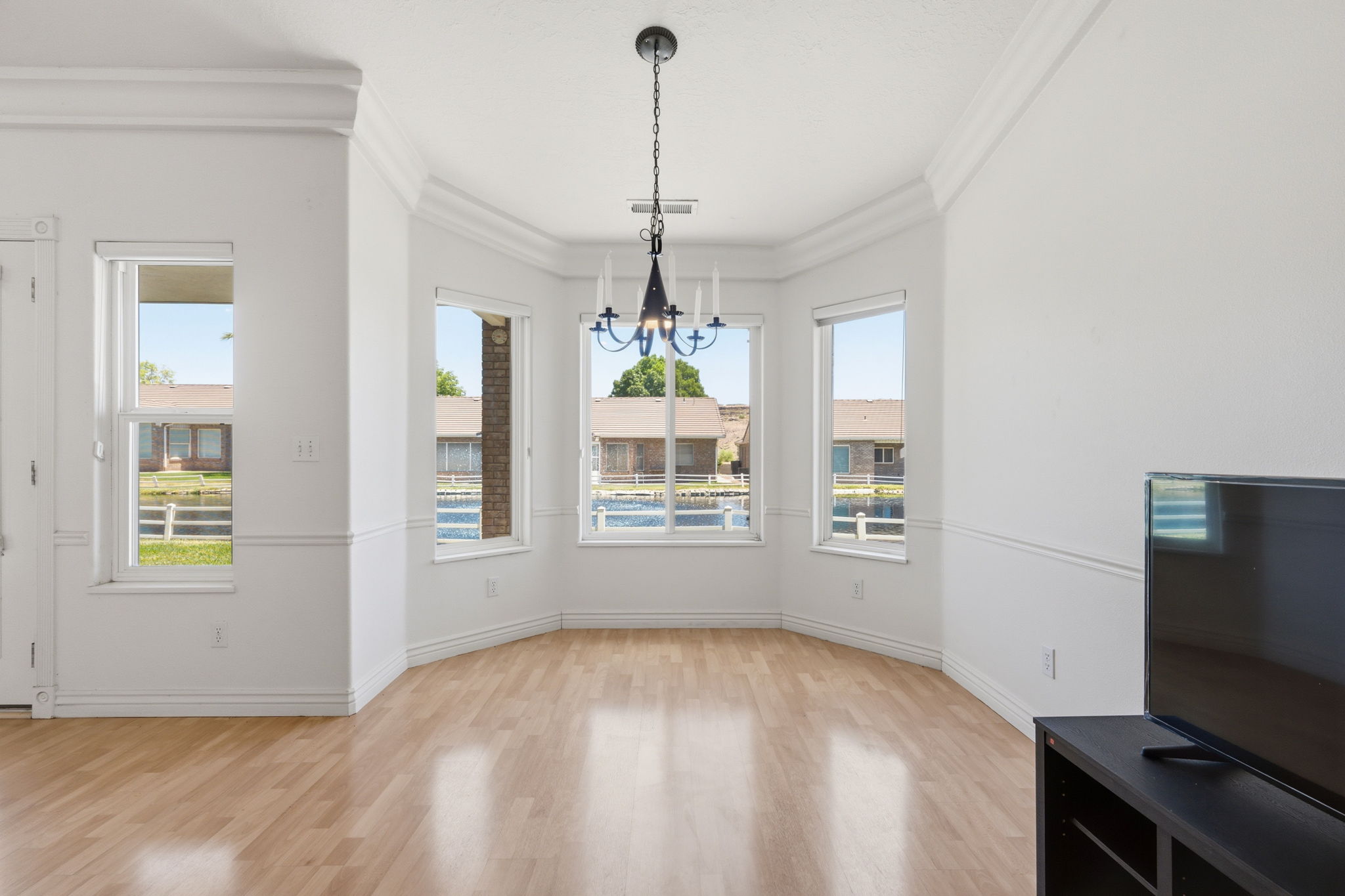Bay window dining area featuring a black chandelier, crown molding, chair rail molding, and wood-finish flooring