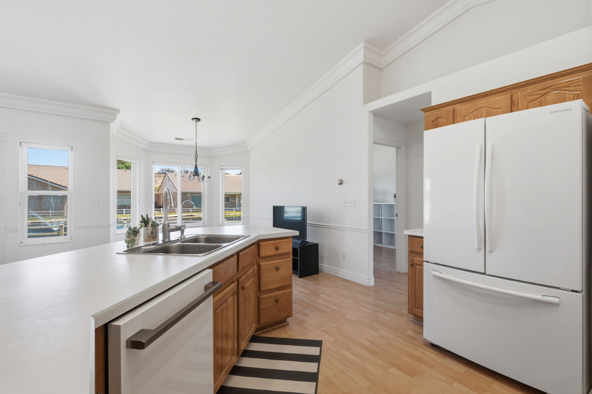 Kitchen featuring light wood-finish flooring, white countertops, dual basin sink, wood cabinetry, and a bay window