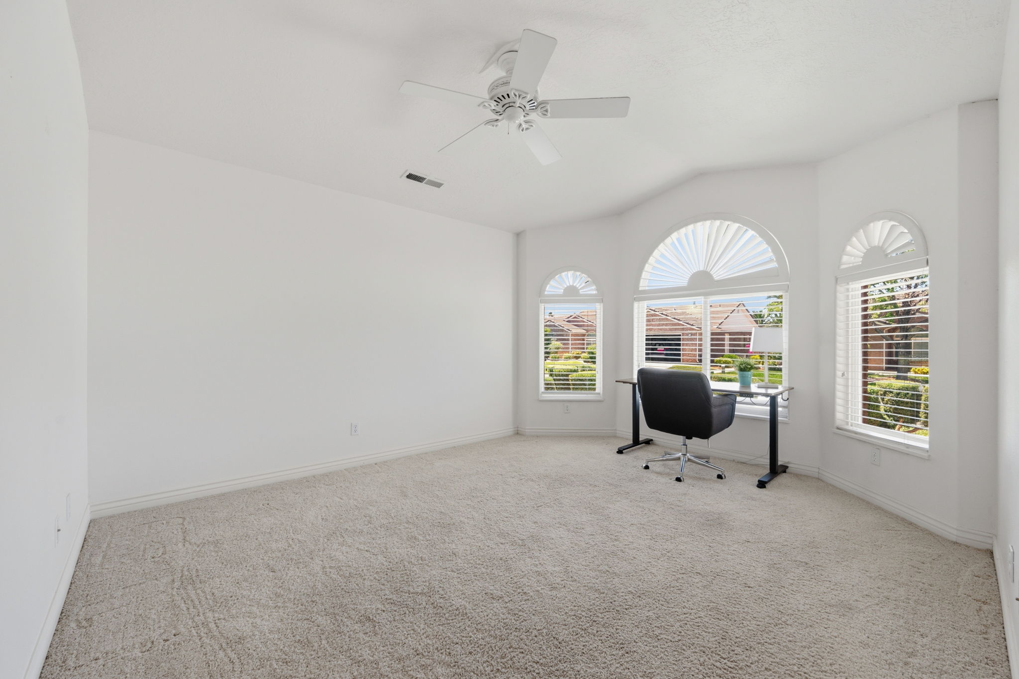 Carpeted room featuring multiple arched windows with blinds, a vaulted ceiling, and a ceiling fan