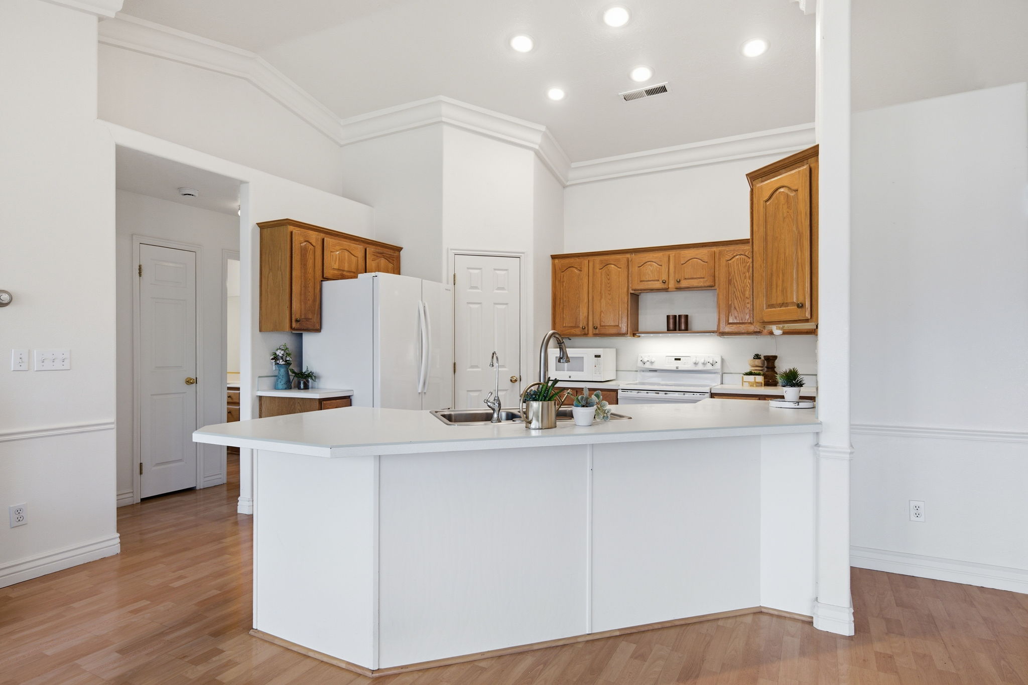 Kitchen featuring wood-finish flooring, white cabinetry, a kitchen island with sink, white appliances, and recessed lighting