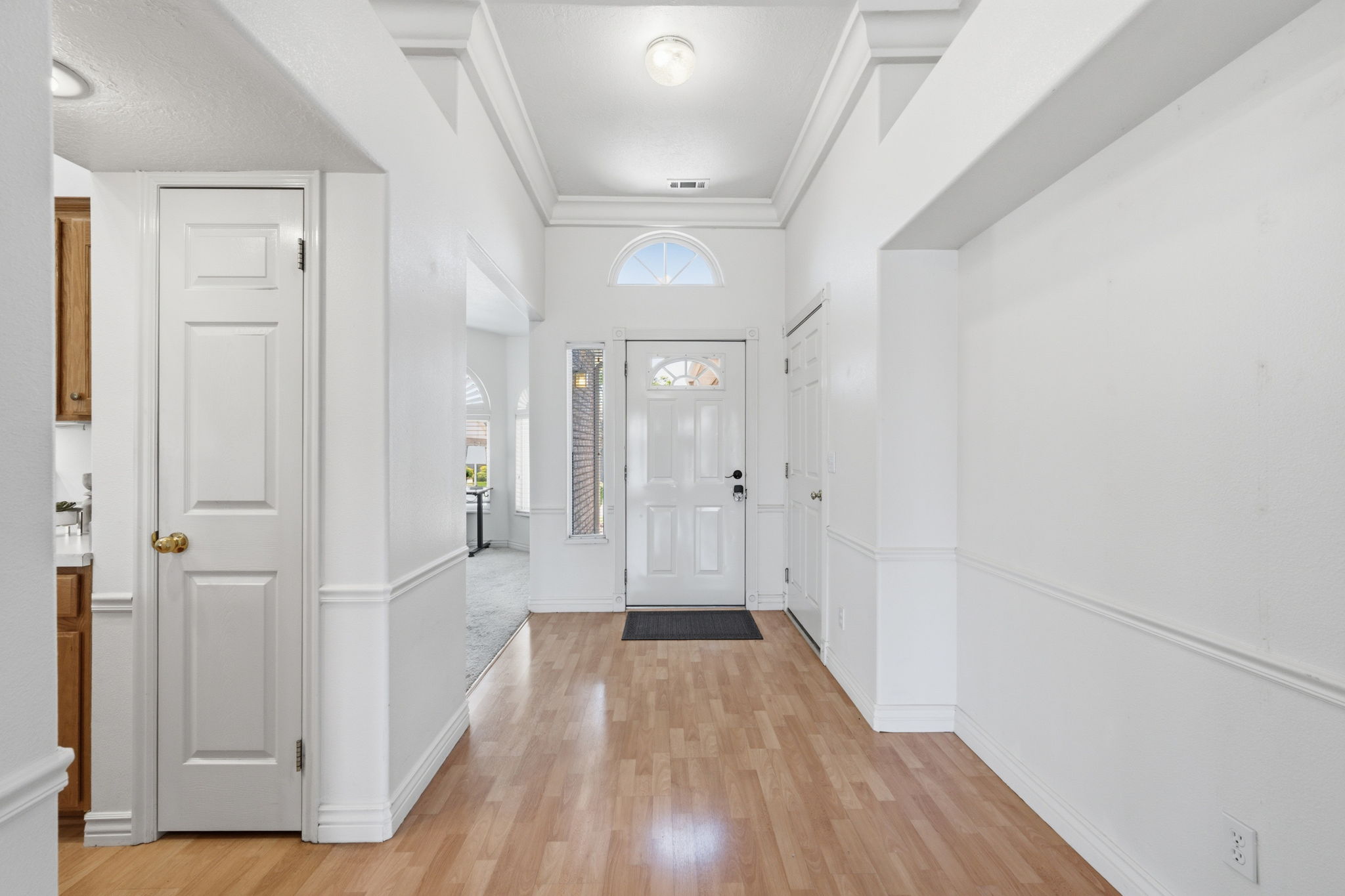 Entryway with wood-finish flooring, white paneled walls, and crown molding