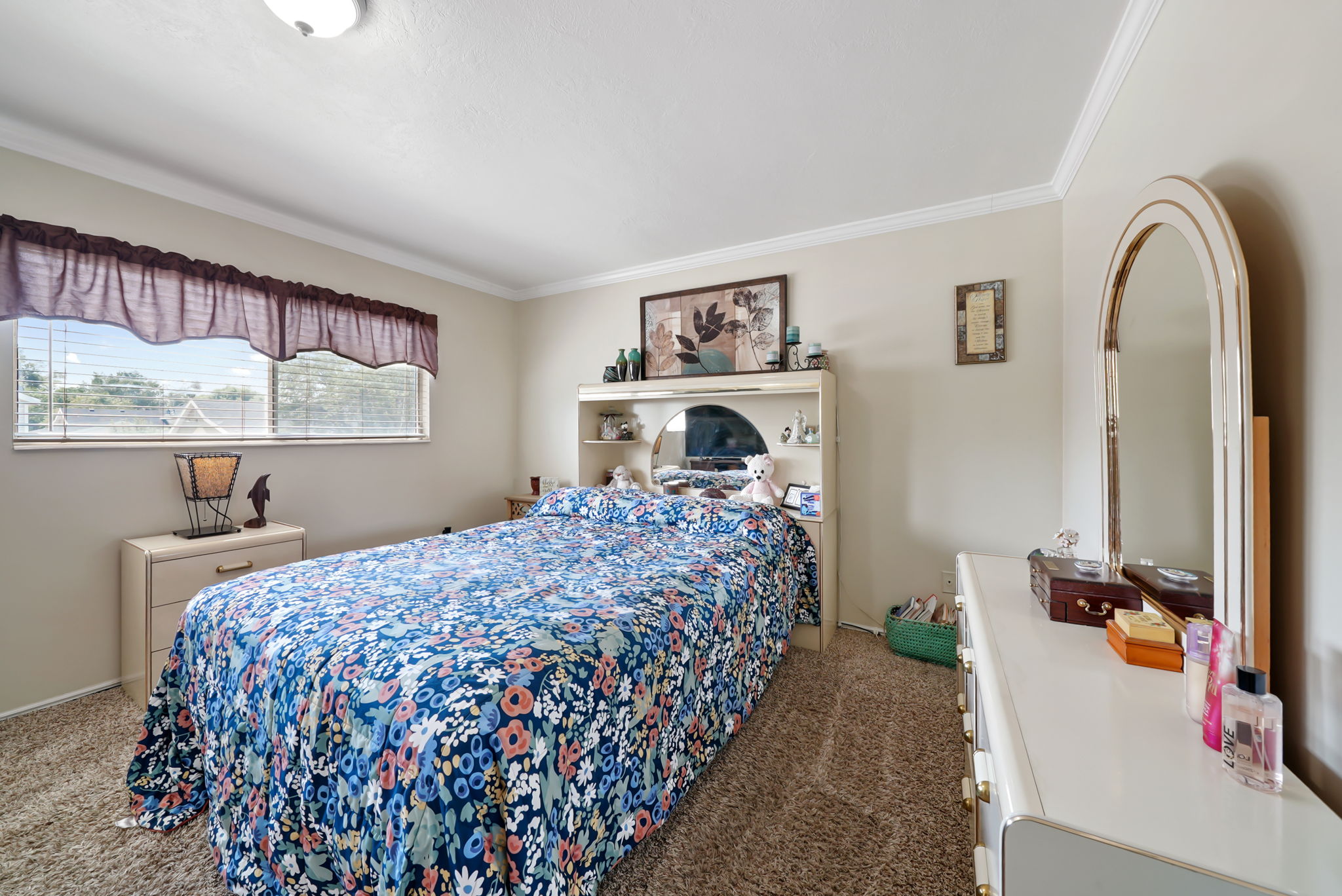 Carpeted bedroom featuring a large window with blinds, crown molding, and a built-in headboard with integrated shelving