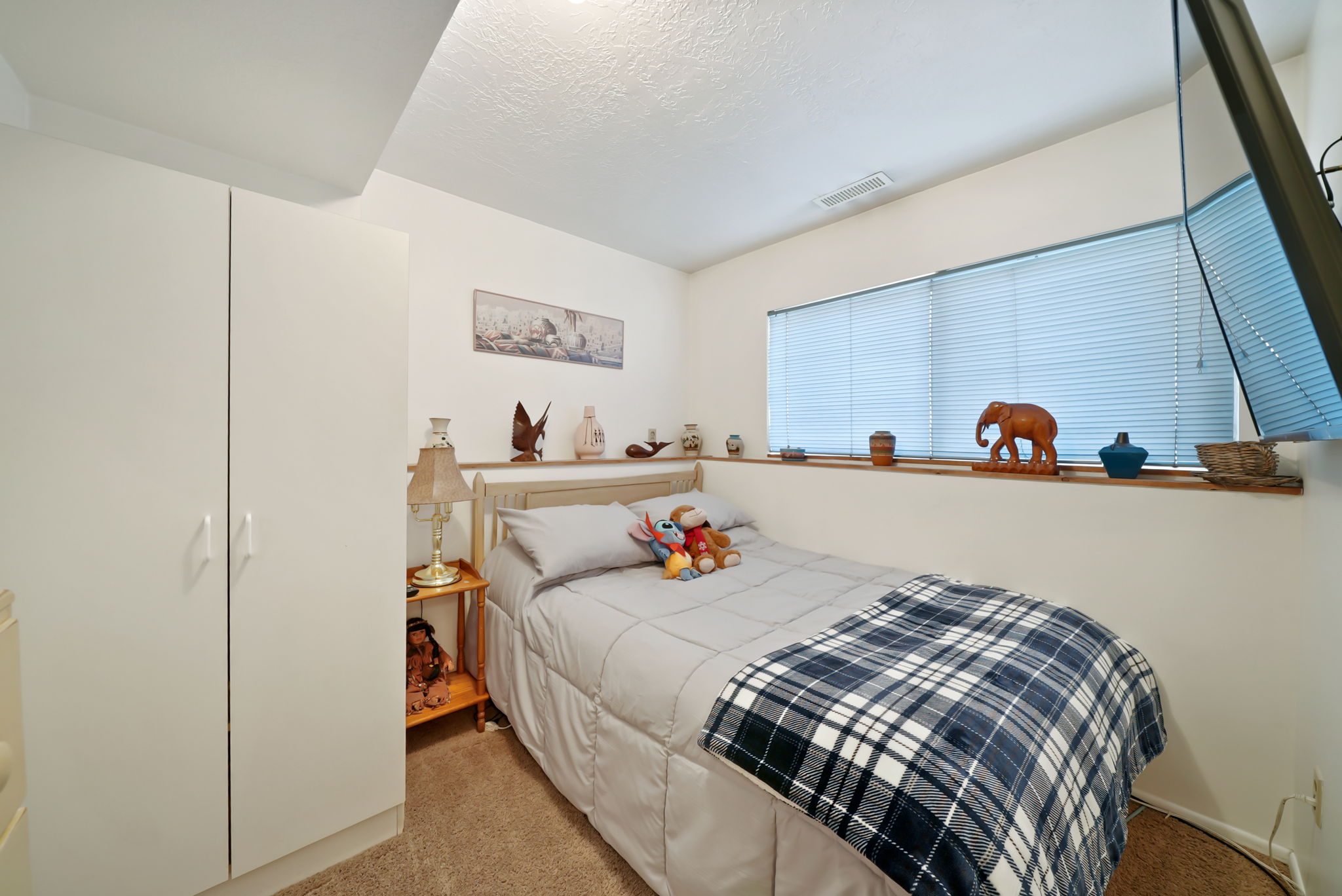 White built-in cabinetry, neutral-toned wall paint, light-colored carpet, and a window with horizontal blinds