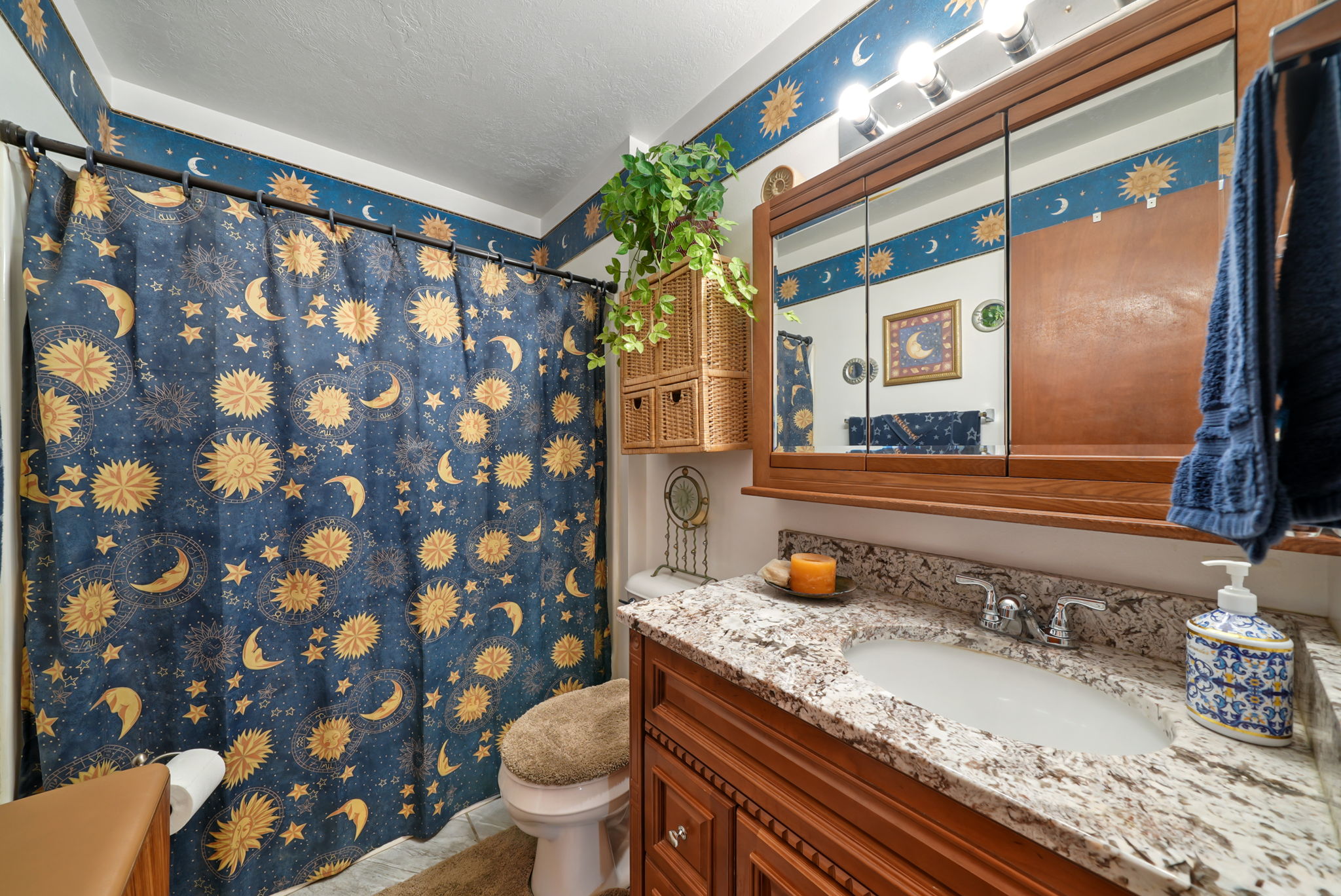 Bathroom featuring a granite-style countertop, integrated sink, wood-finish vanity with paneling, and an overhead mirrored medicine cabinet with integrated lighting