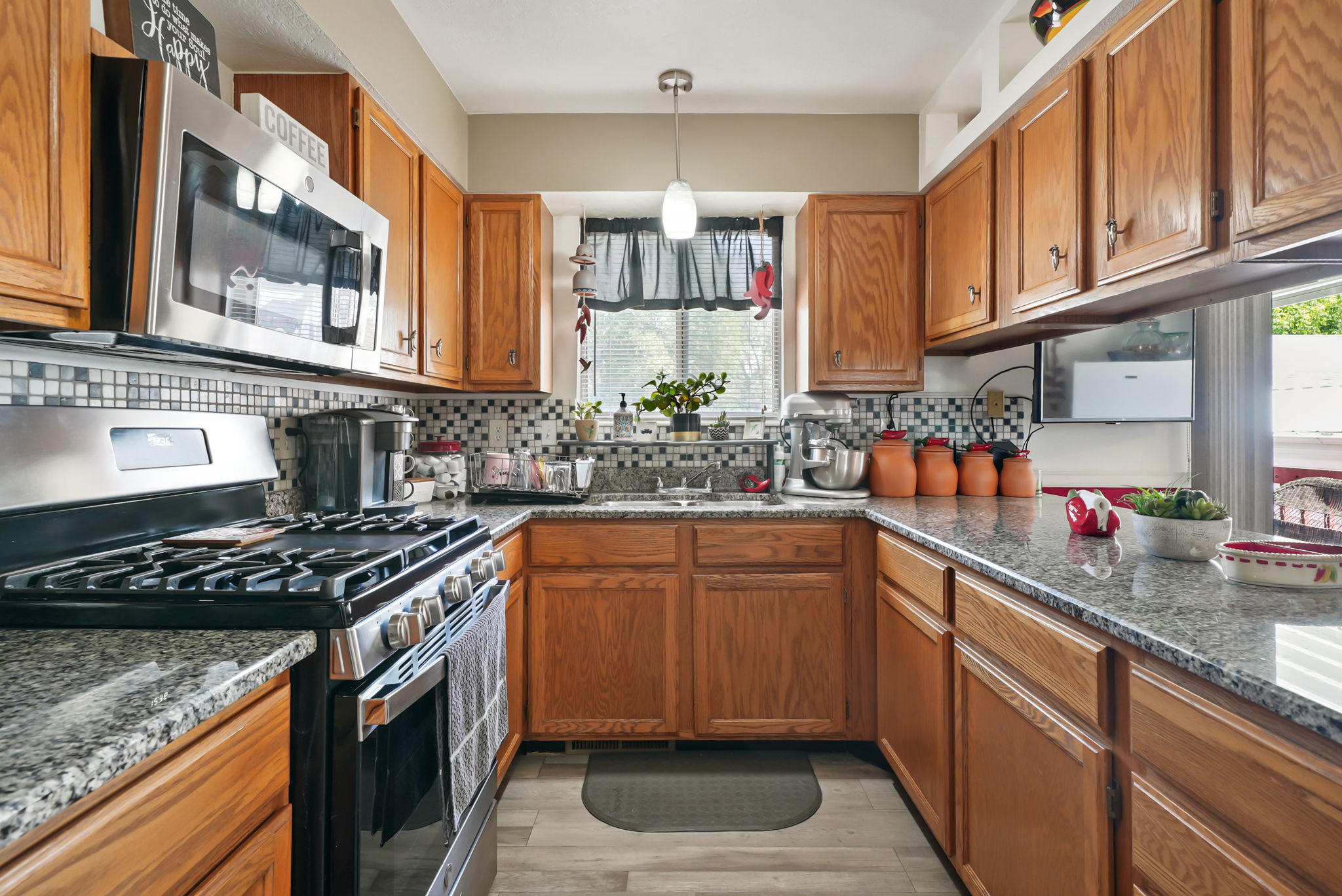 Kitchen featuring a mosaic tile backsplash, wood-finish cabinetry, stainless steel appliances, granite countertops, and wood-finish flooring