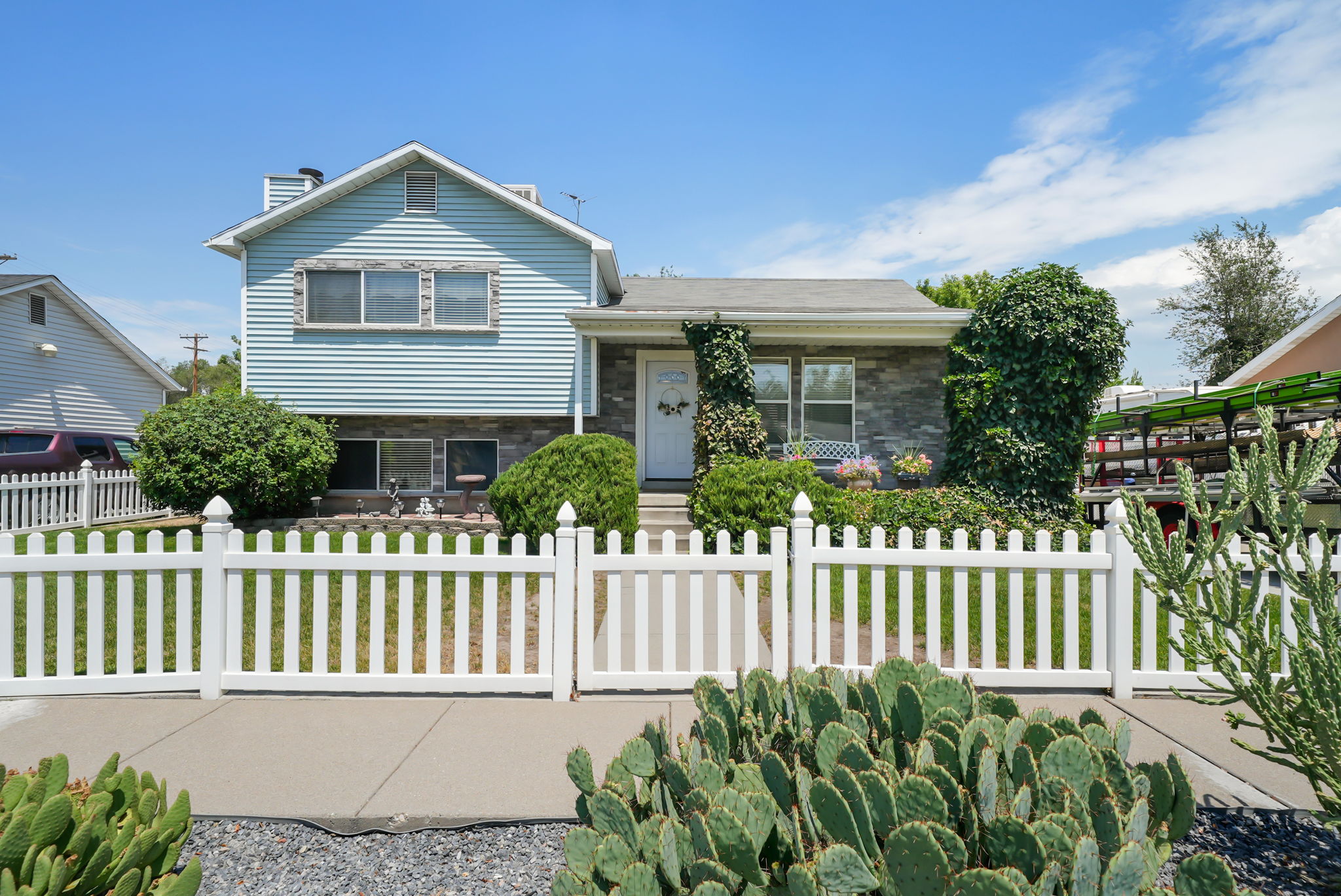 Front exterior featuring a white picket fence, a stone facade, blue horizontal siding, and mature landscaping