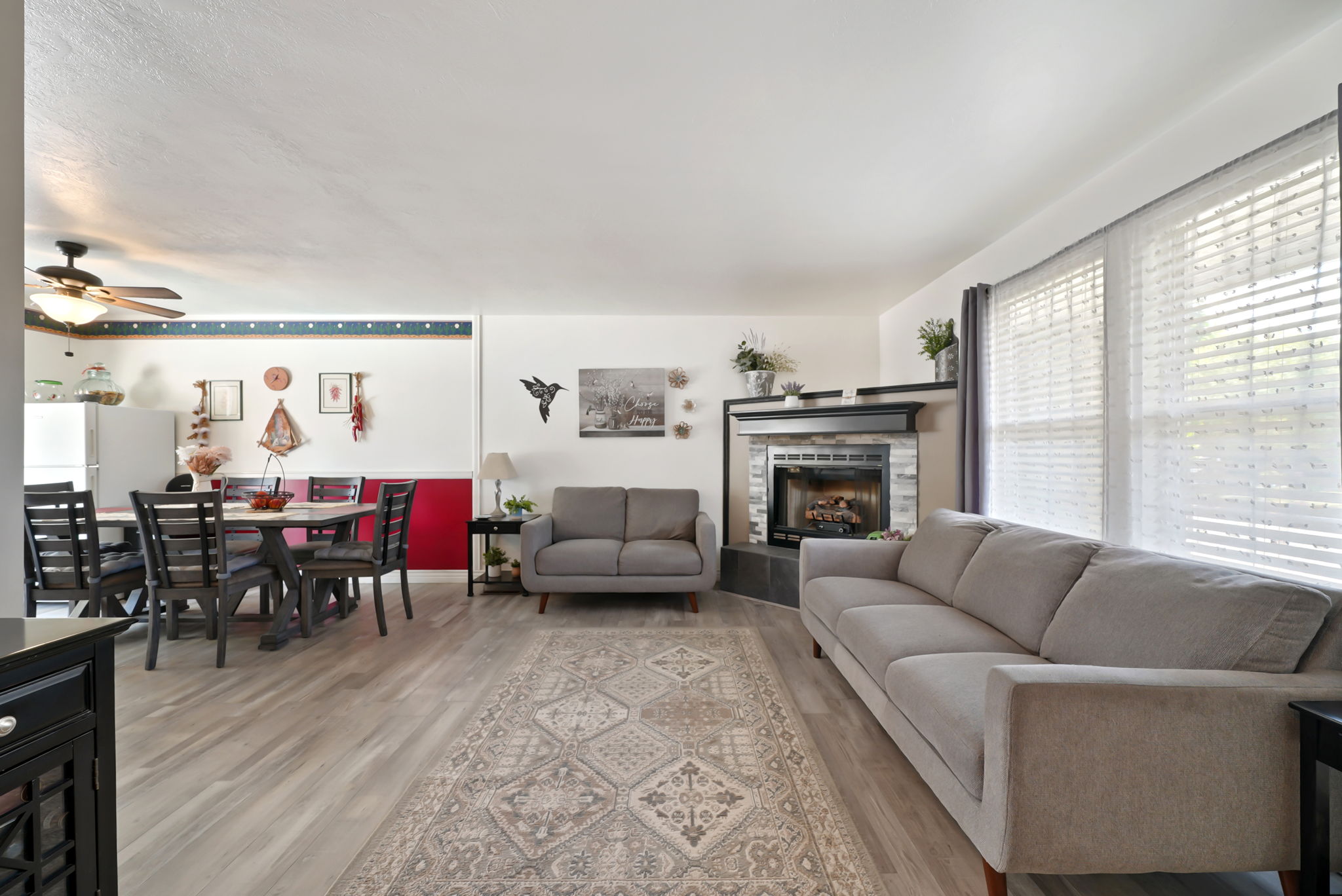 Living area featuring wood-finish flooring, a tiled fireplace with a dark mantel, and multiple windows with blinds