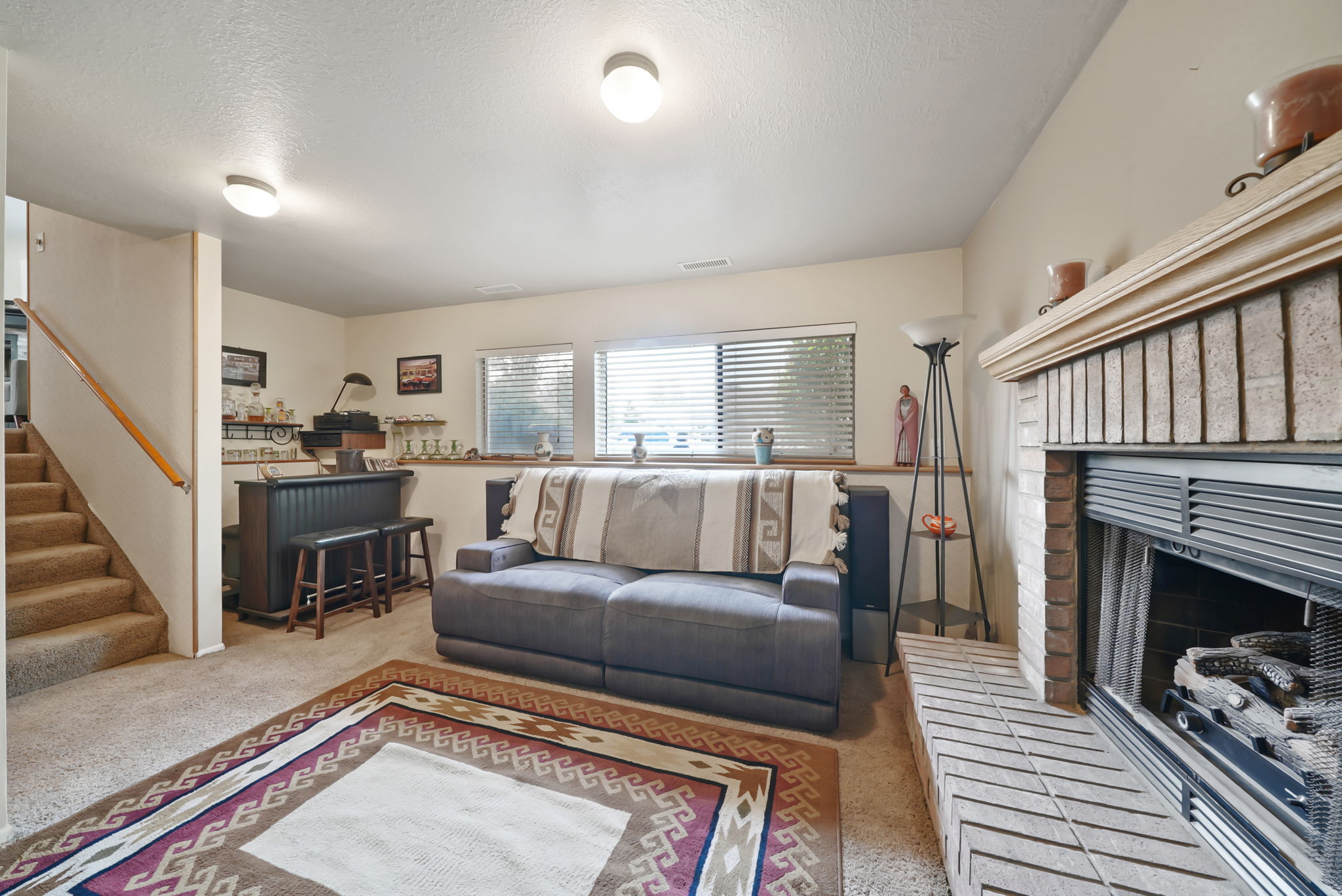 Living area featuring a brick-surround fireplace with a hearth, multiple windows, a built-in bar, and carpeted stairs with a wood handrail