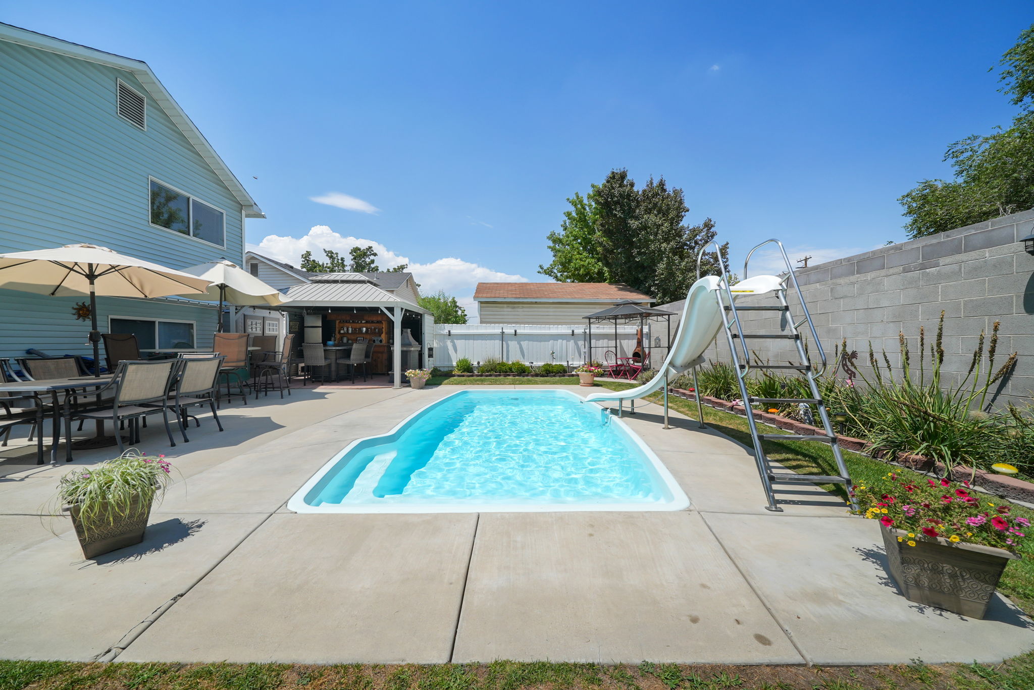 Backyard oasis featuring a swimming pool with integrated steps and slide, surrounded by extensive concrete patio decking
