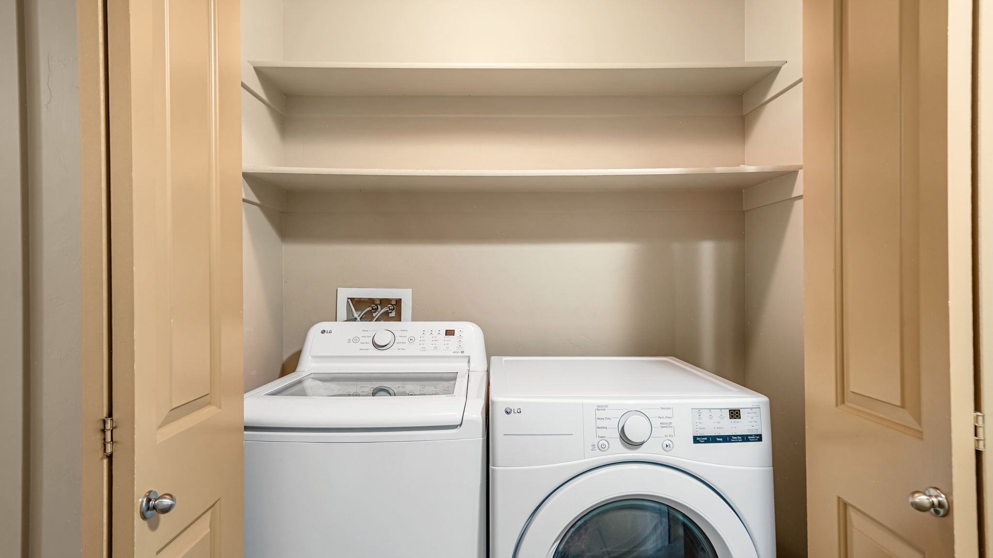 Dedicated laundry closet featuring a top-load washer, front-load dryer, and two integrated storage shelves