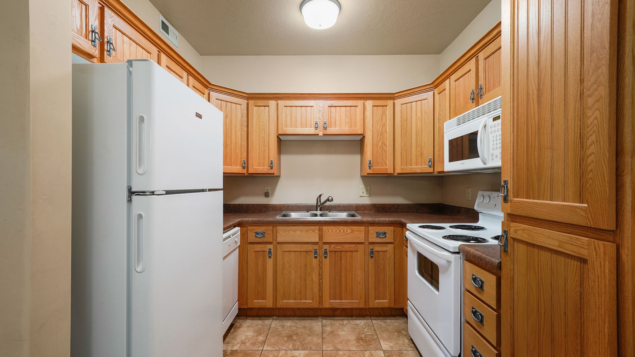 Kitchen featuring wood cabinetry, laminate countertops, a double basin sink, and tile flooring
