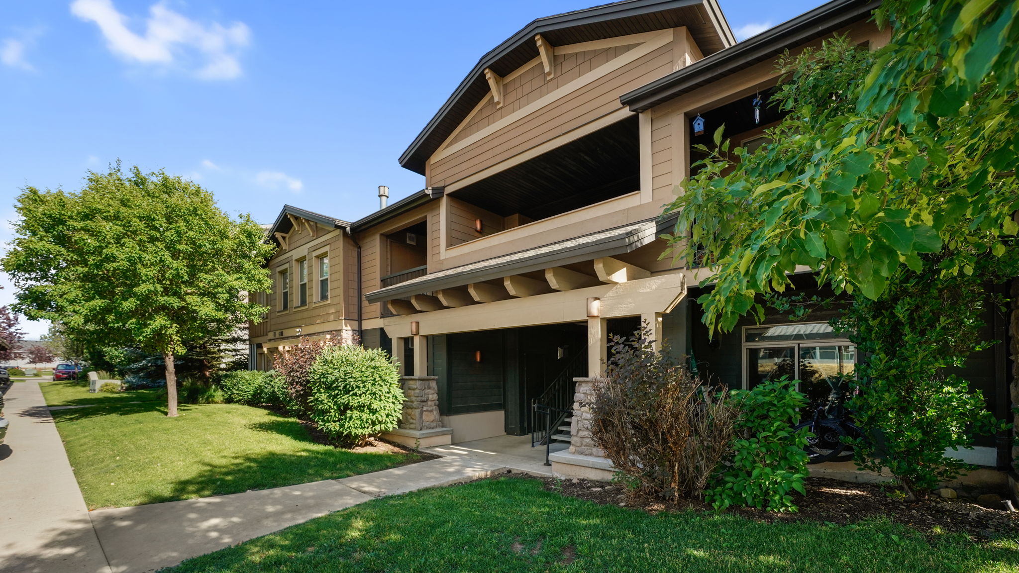 Multi-story dwelling featuring brown siding, stone column accents, a covered entry, and an upper-level balcony