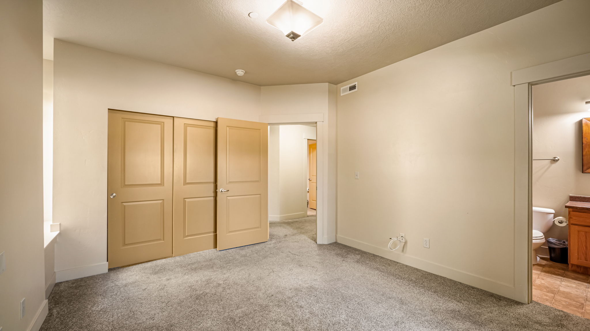 Carpeted room featuring a built-in closet with four panel doors, a ceiling-mounted light fixture, and an entryway into a bathroom with a wood vanity and a toilet