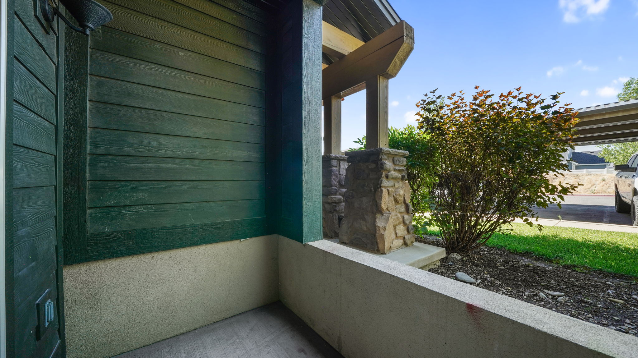 Entryway with dark green horizontal siding and a stone-clad column