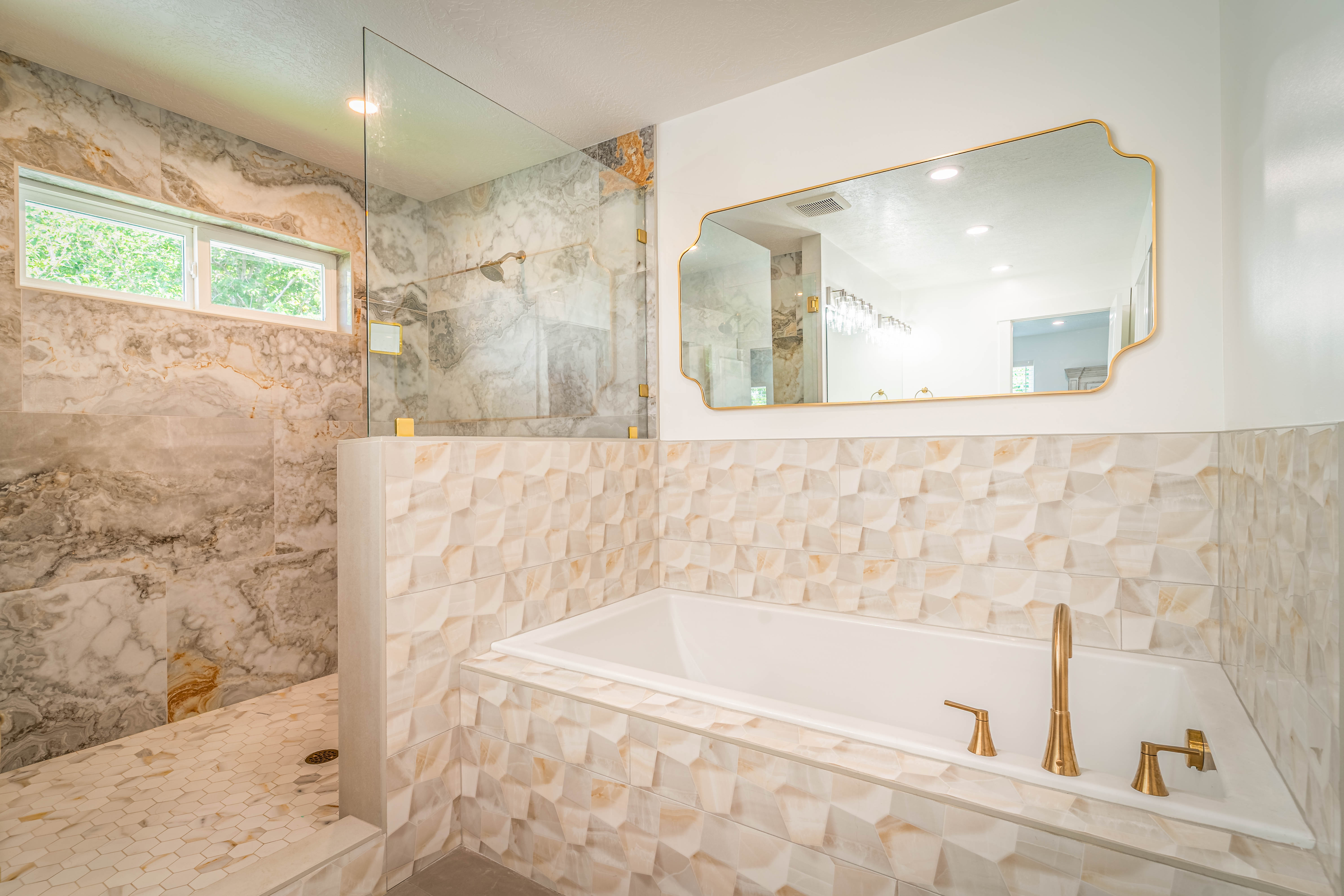 Freestanding soaking tub with gold-tone fixtures and textured tile surround