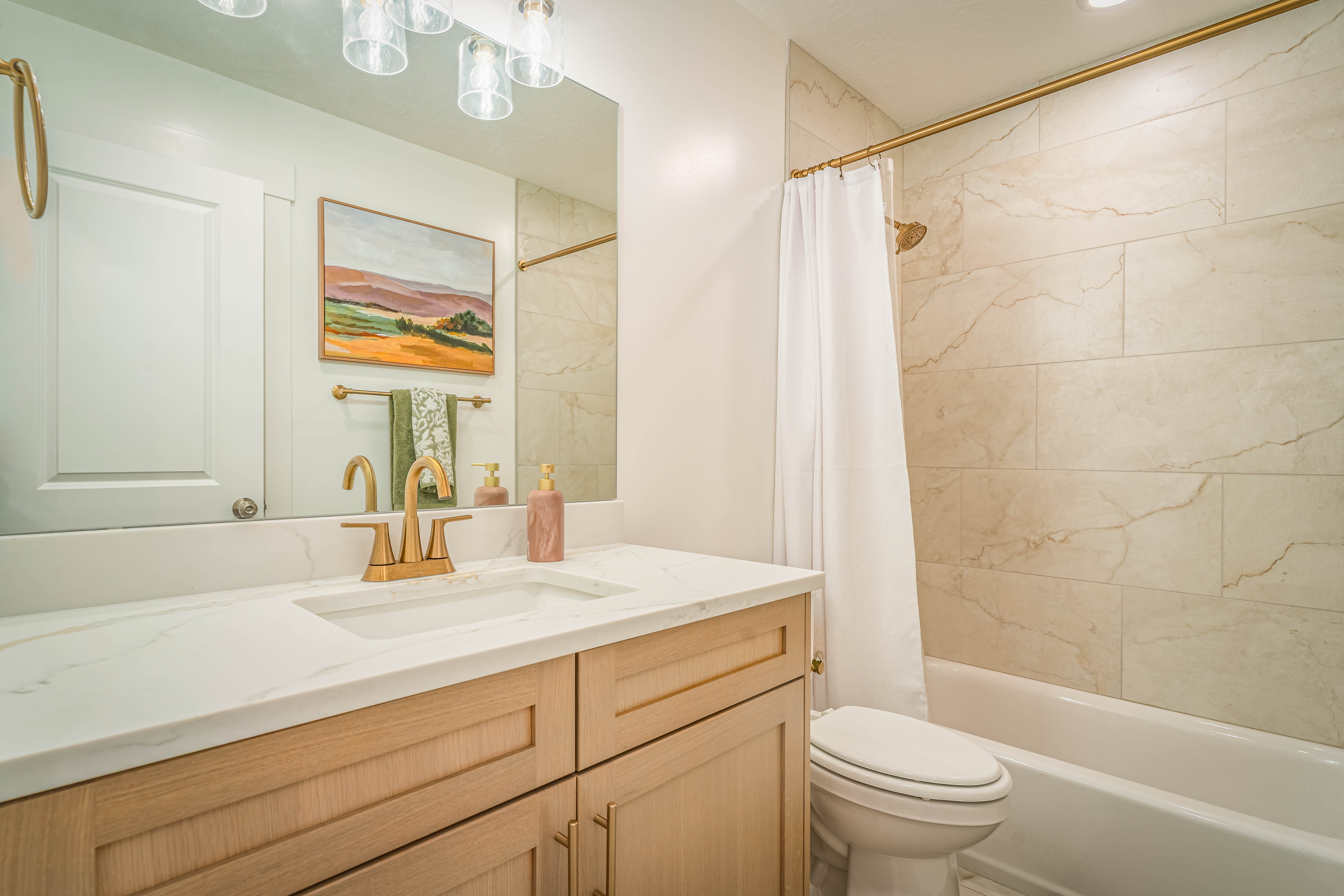 Bathroom featuring a wood-finish vanity with a white countertop, an undermount sink, and a gold-finish faucet