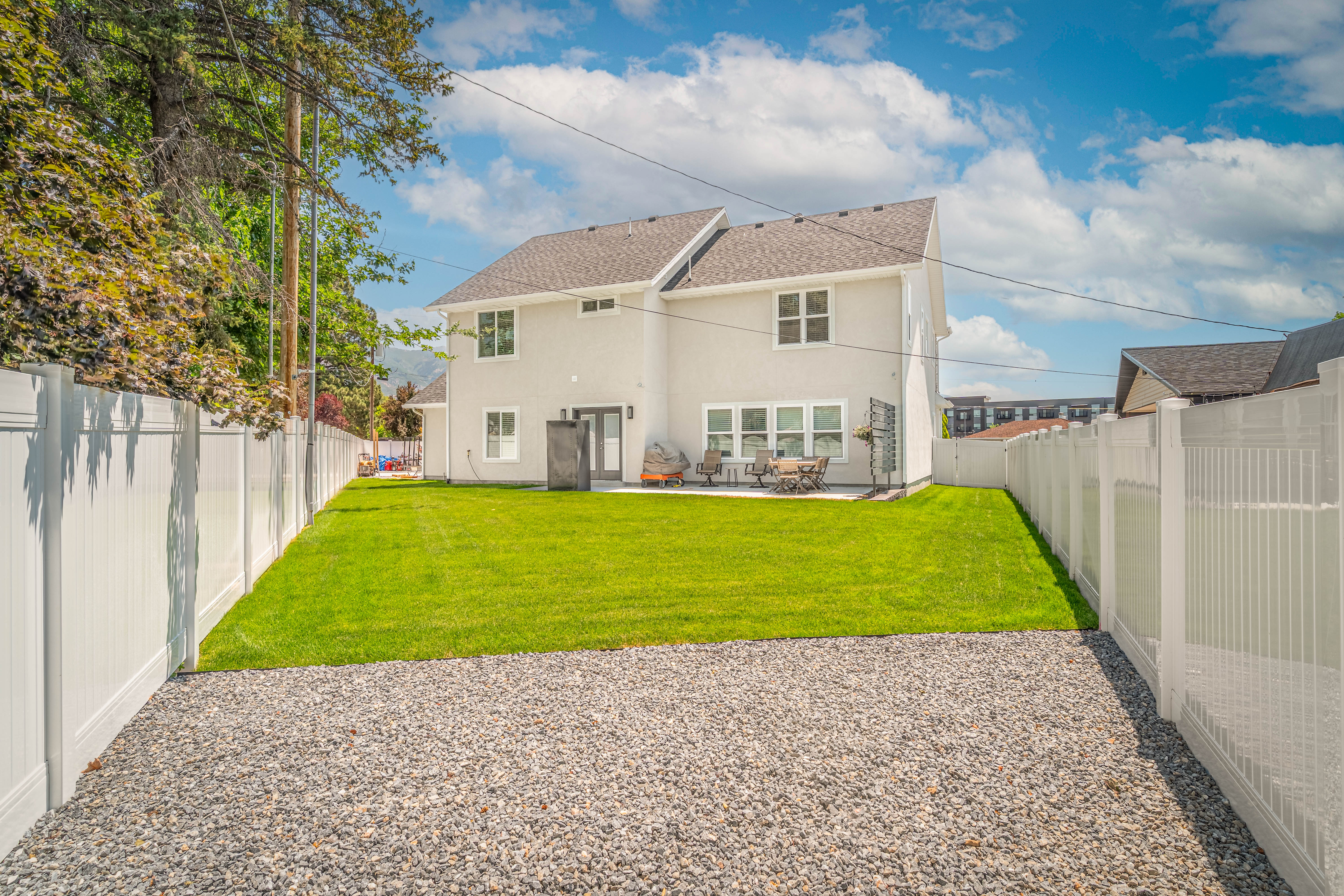 Expansive rear yard featuring a gravel pathway, manicured lawn, and white privacy fencing