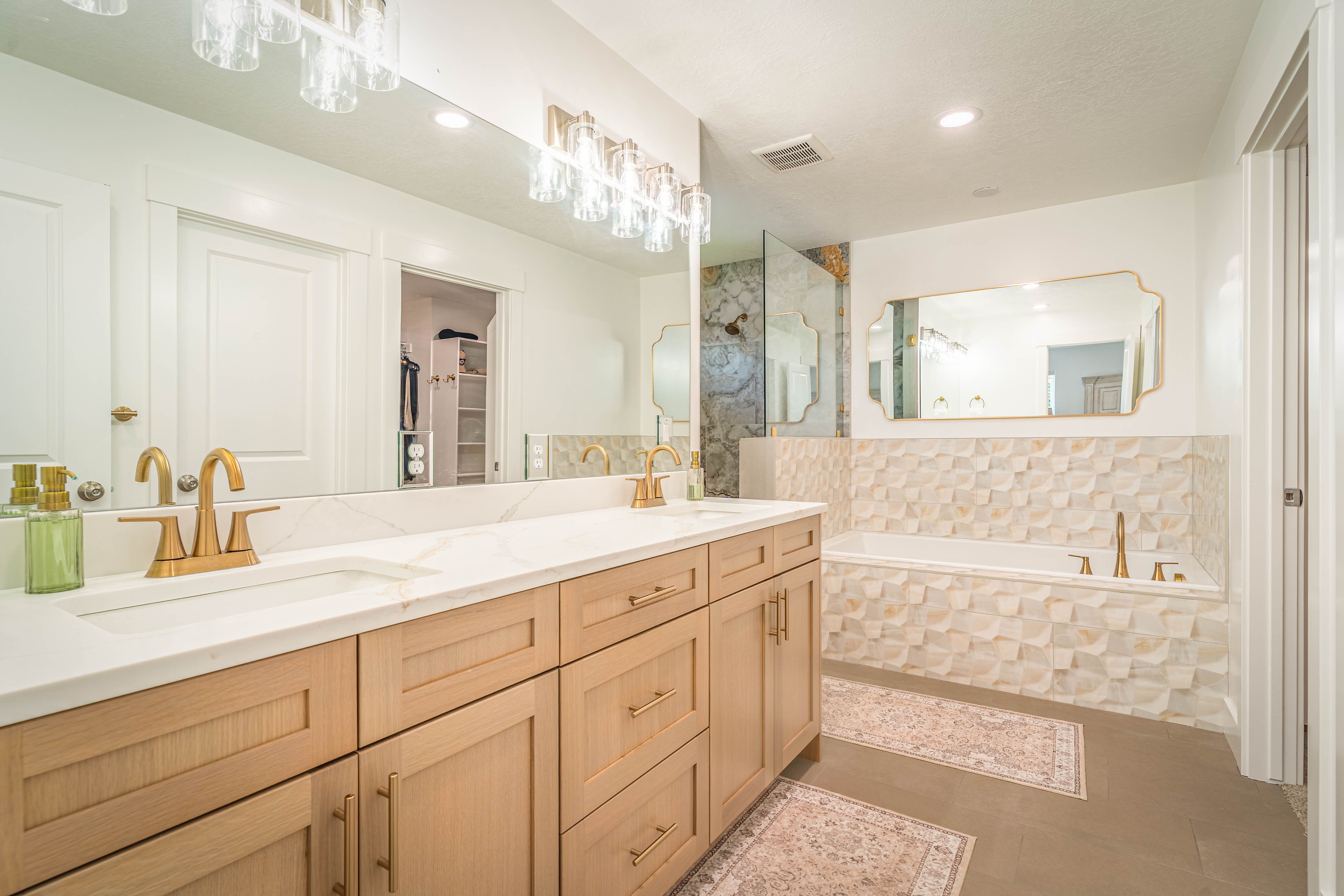 Dual vanity with light wood-finish cabinetry, white countertops, and gold-finish fixtures