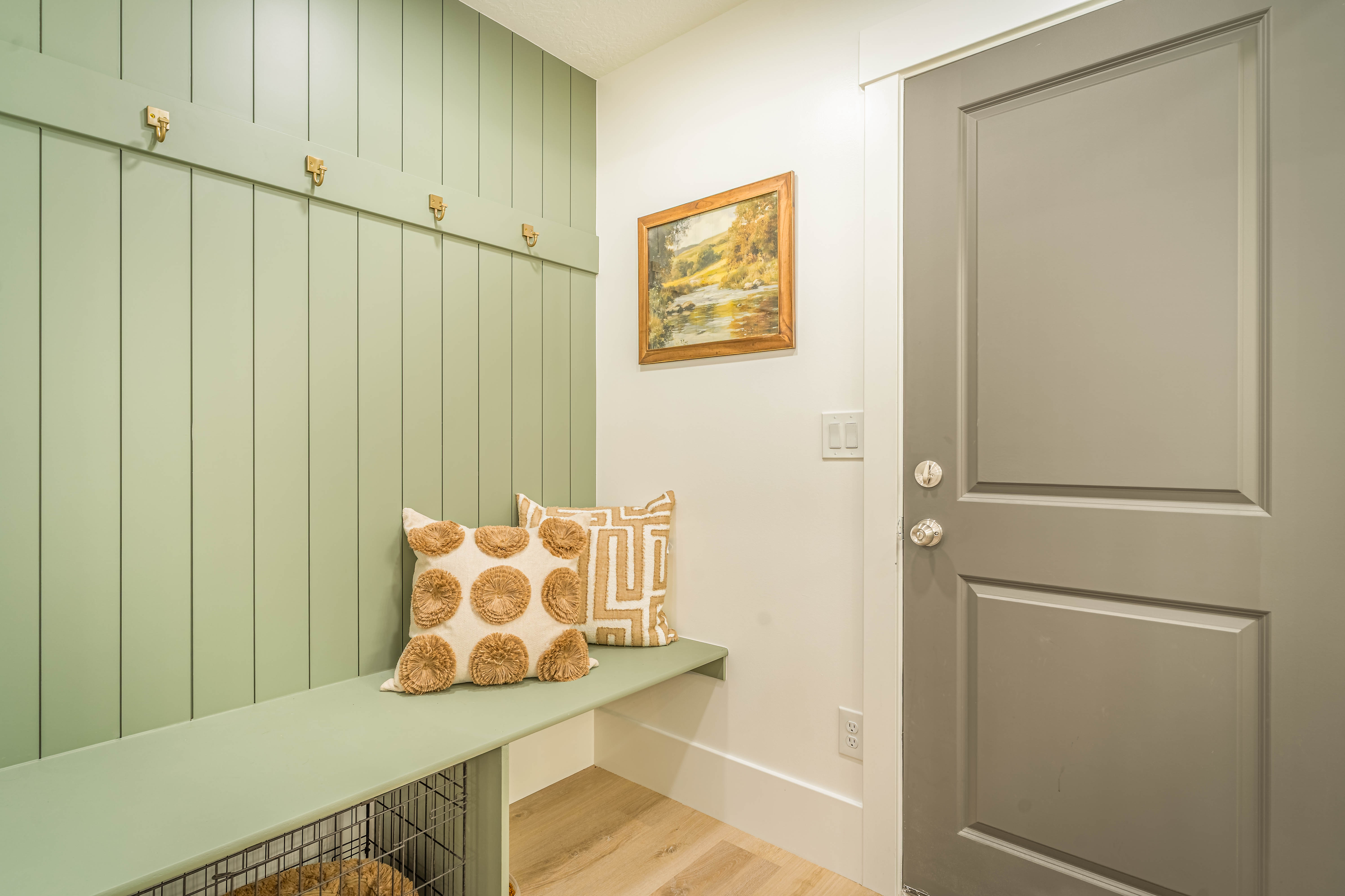Entryway mudroom with custom board and batten wall paneling, built-in bench seating, multiple brass coat hooks, and light wood-finish flooring