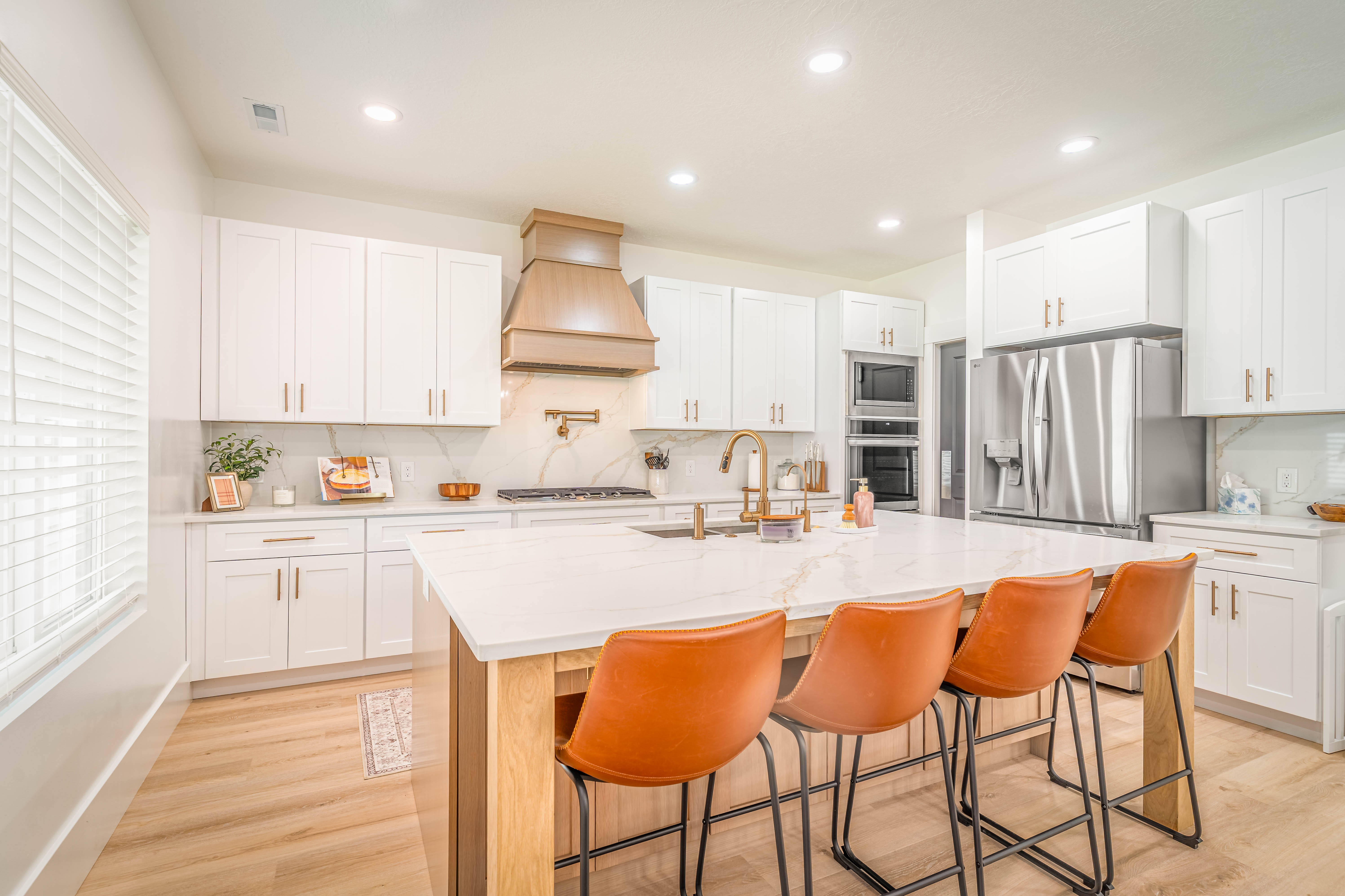 Gourmet kitchen featuring a large central island with seating, white shaker cabinetry, stainless steel appliances, and wood-finish flooring