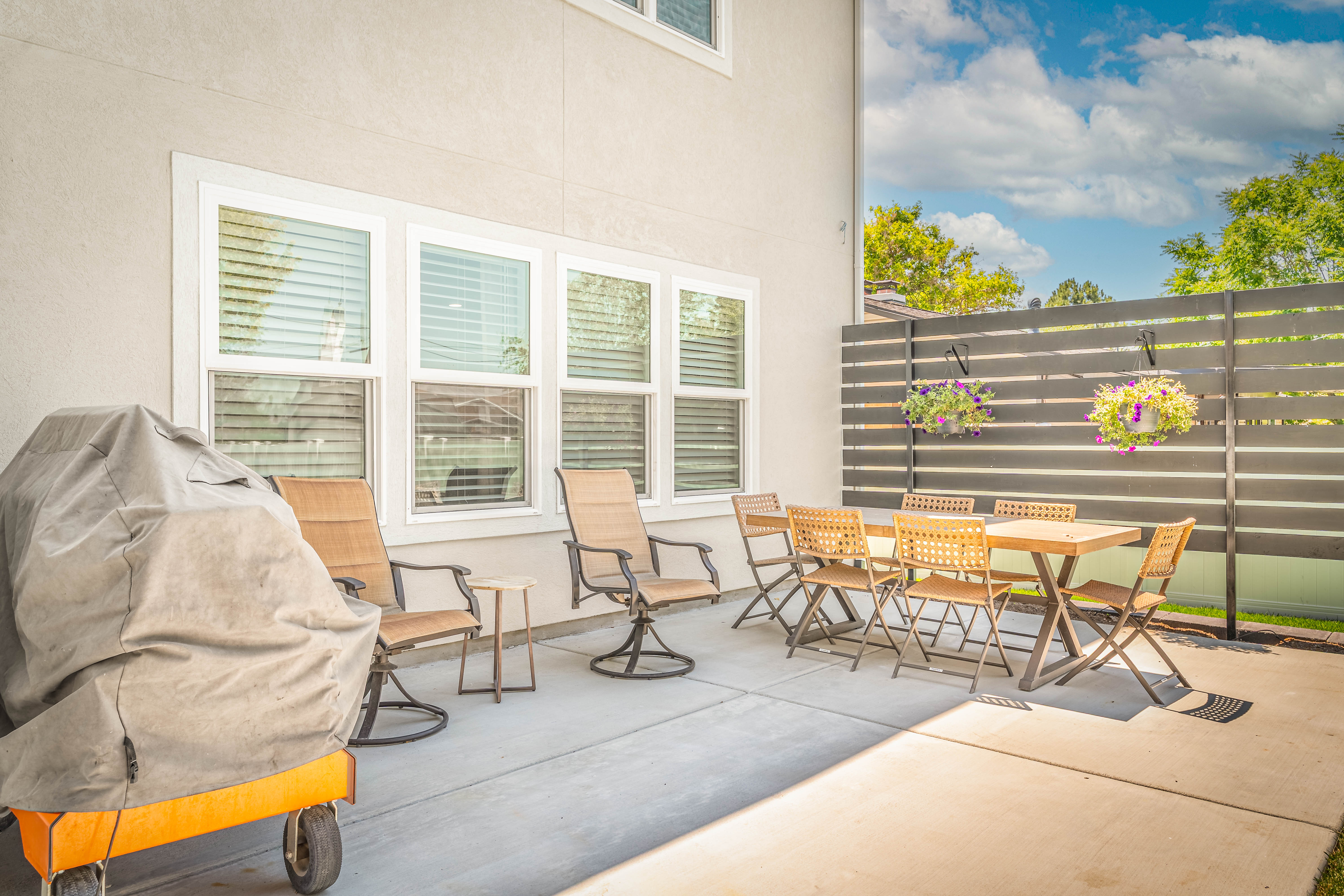 Spacious concrete patio featuring a horizontal slat privacy fence, white-framed windows with blinds, and a light-colored stucco exterior