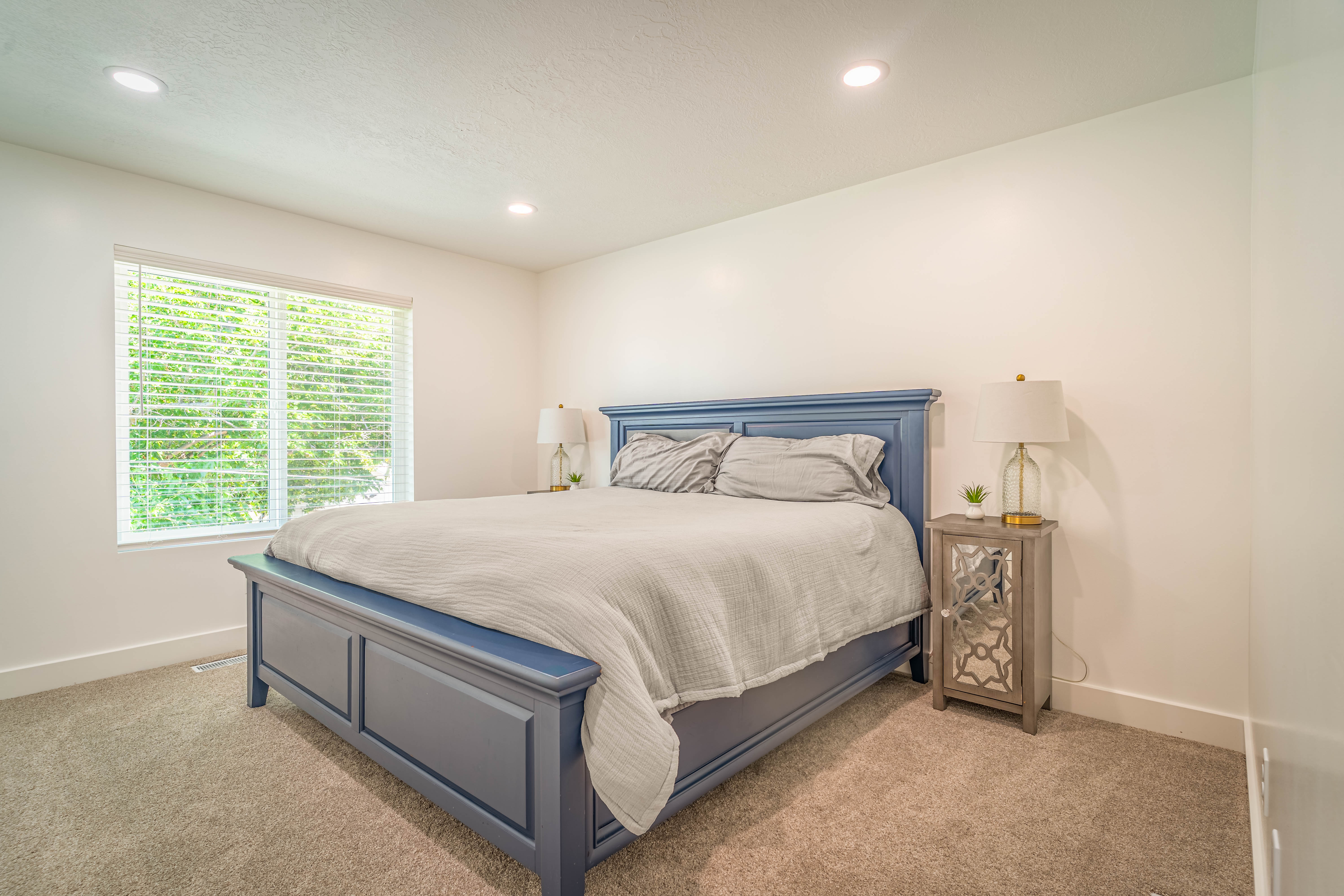 Bedroom featuring neutral carpeting, white walls, a large window with horizontal blinds, and recessed ceiling lighting