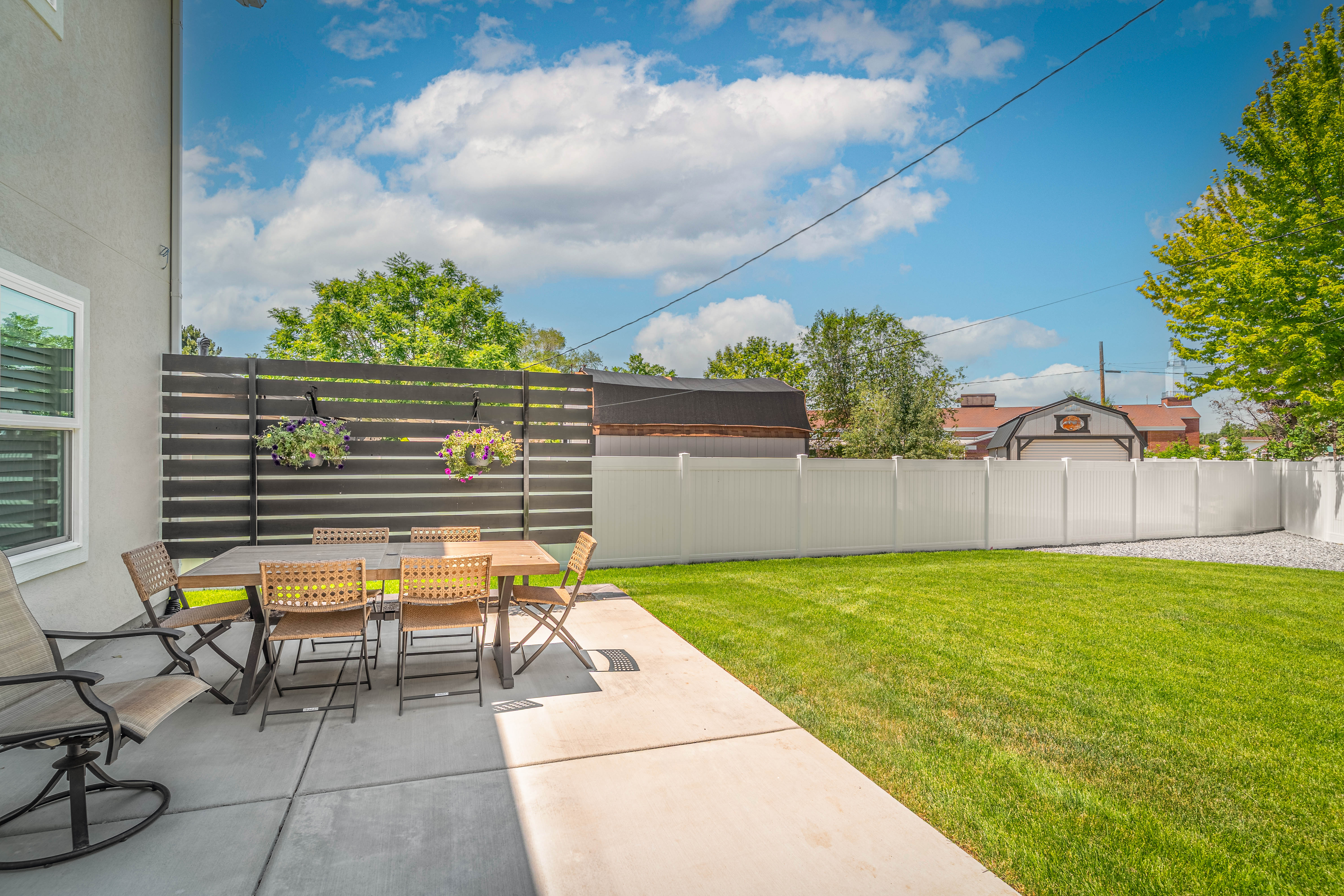 Expansive backyard featuring a concrete patio, a privacy screen with horizontal slats, and a white vinyl fence