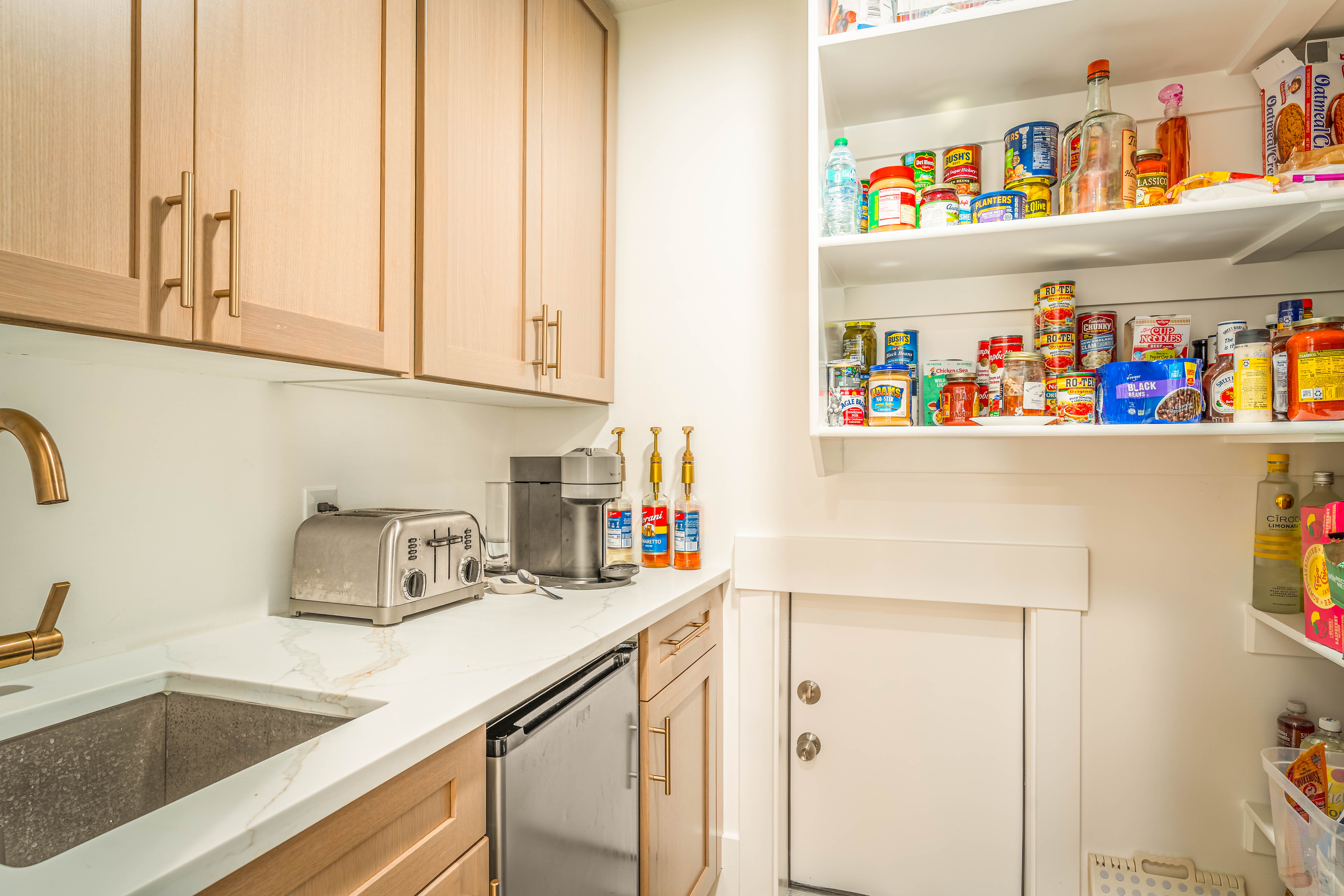 Kitchenette featuring shaker-style upper and lower cabinetry with matte gold hardware, a built-in beverage refrigerator, and a gold-tone faucet