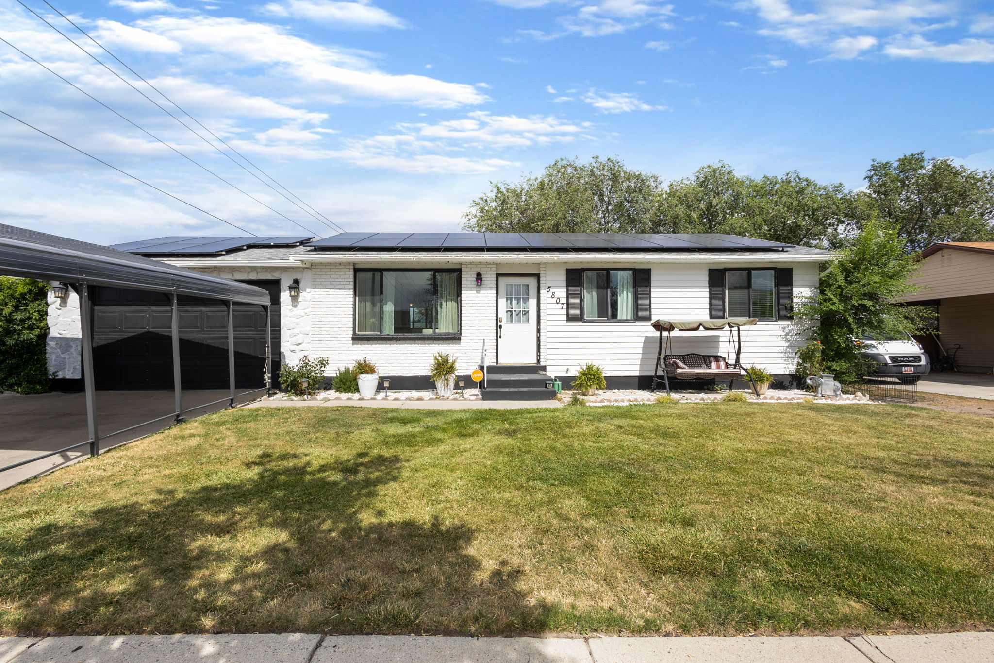 Single-story residence featuring a white brick and siding facade, black window frames with shutters, a covered carport, and rooftop solar panels