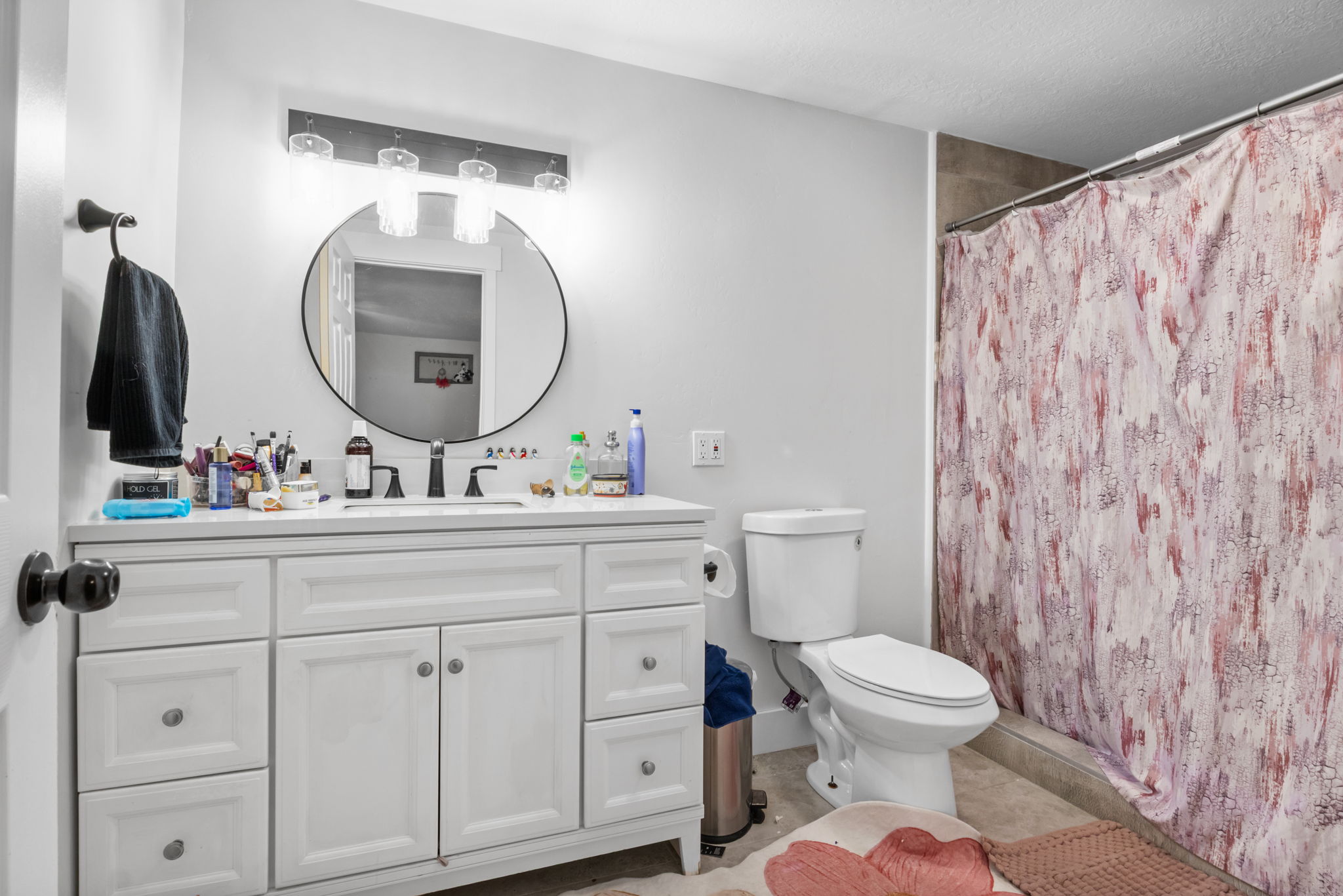 Bathroom featuring a white vanity with integrated sink, a circular mirror, and a three-light fixture