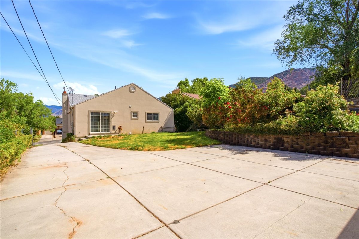 Expansive concrete driveway with a retaining wall, mature landscaping, and mountain backdrop