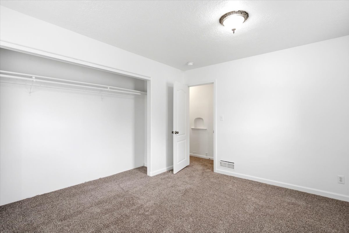 Carpeted interior room featuring a white door, overhead ceiling light fixture, white walls, and a closet with wire shelving
