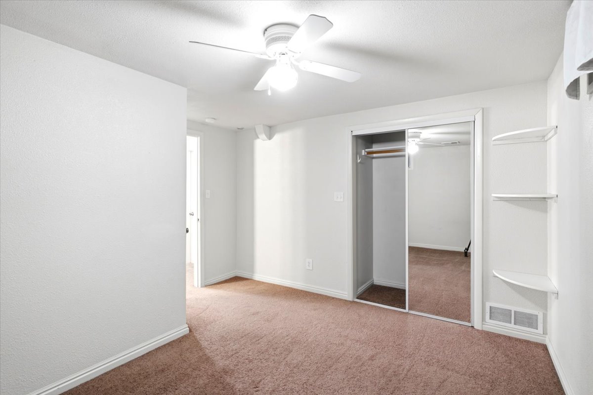 Carpeted room featuring a ceiling fan, mirrored closet doors, and built-in shelving