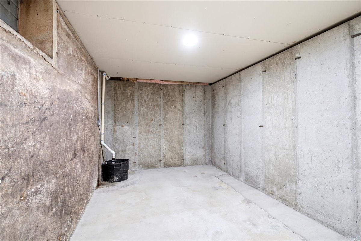 Unfinished basement featuring poured concrete walls, a concrete floor, and a sump pump system