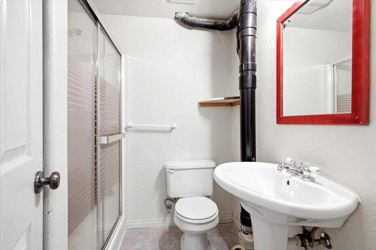 Bathroom featuring a pedestal sink with chrome fixtures, a toilet, and a stand-up shower with a clear glass enclosure