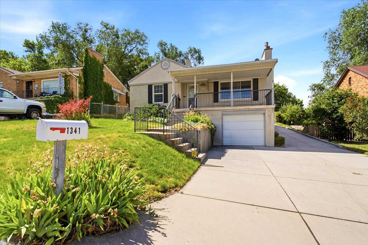 Split-level residence featuring a covered entry porch with black railings, a white garage door, and a concrete driveway