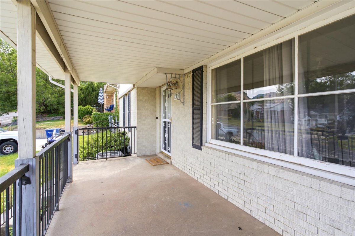 Covered front porch featuring a concrete surface, black metal railing, and white painted brick exterior