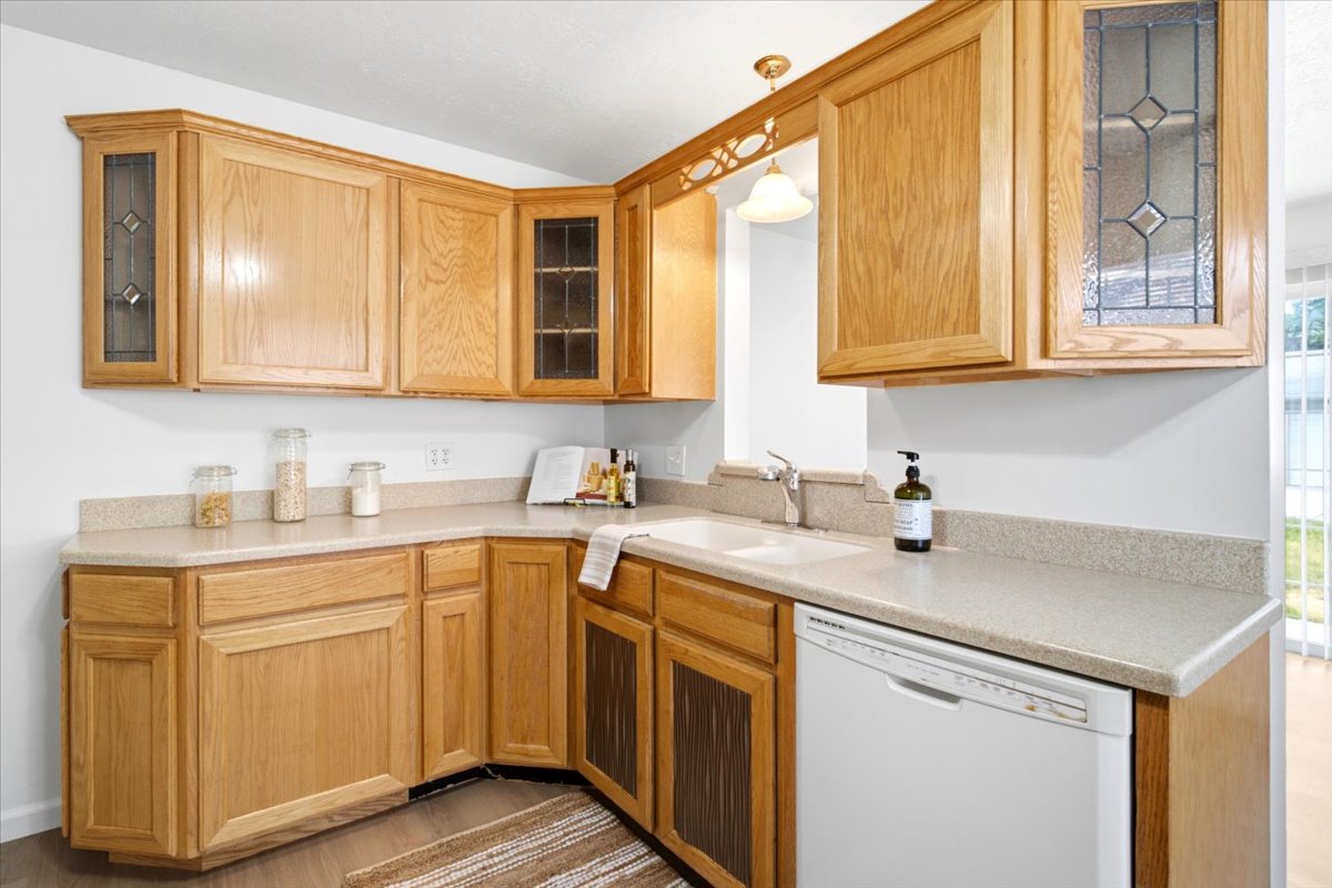 L-shaped kitchen featuring wood cabinetry, integrated white sink, dishwasher, and light-toned countertops