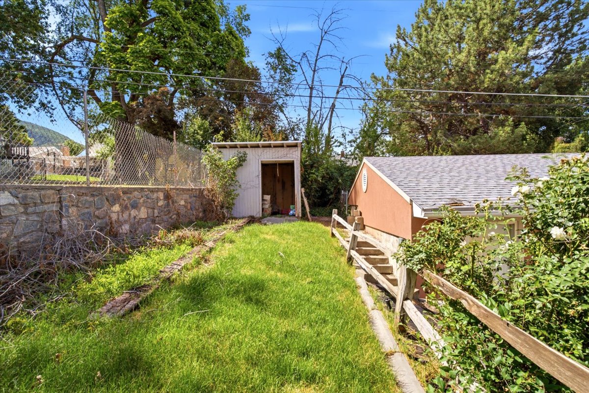 Expansive outdoor space featuring a manicured lawn, a detached storage shed, a stone retaining wall, and mature perimeter trees