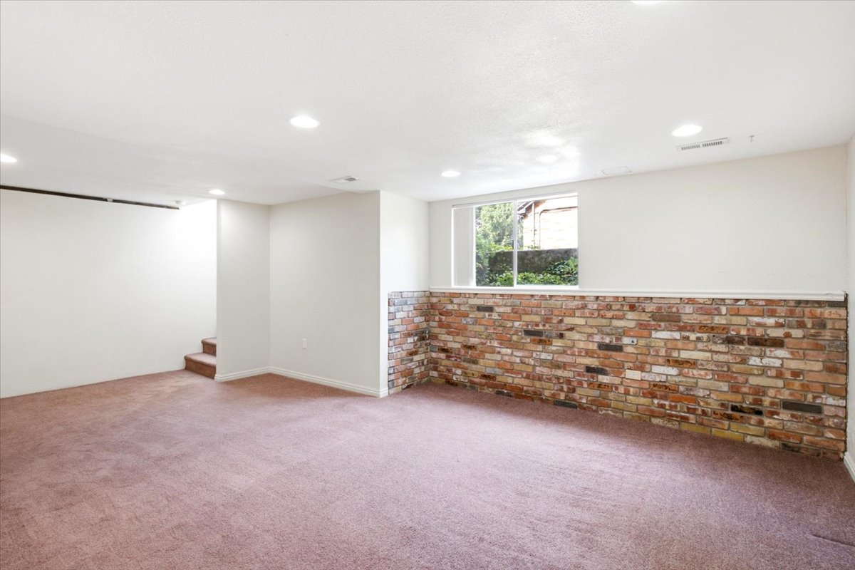 Spacious room featuring a brick accent wall, recessed lighting, and a large window
