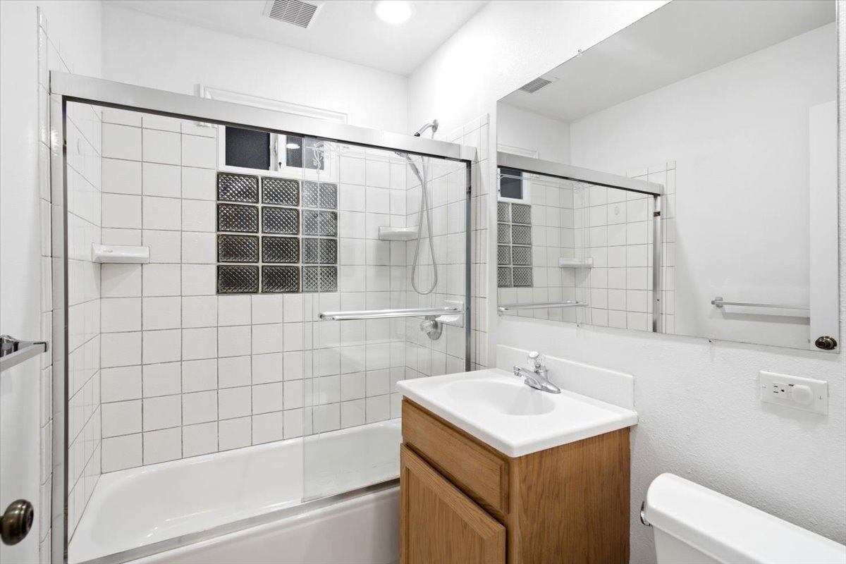 Bathroom featuring a built-in bathtub with shower, glass enclosure, white square tile surround, and a glass block window
