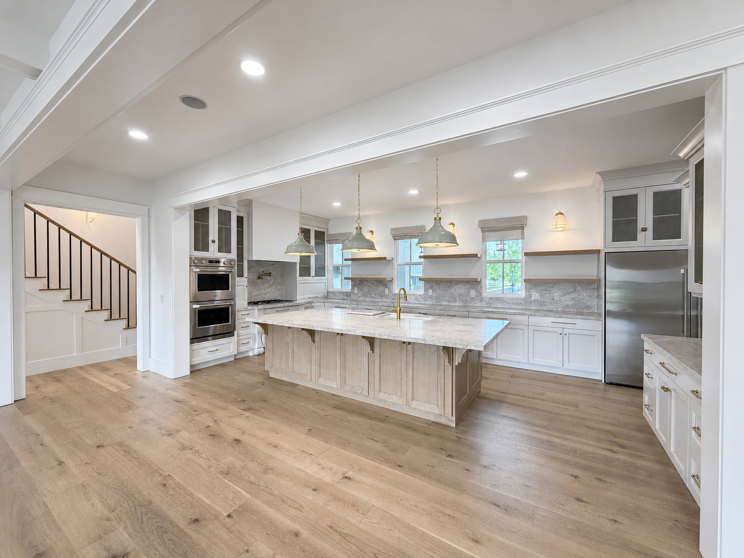 Open-concept kitchen featuring a large wood base island with Taj Mahal leather quartzite stone counters, stainless steel appliances, white cabinetry and engineered wood flooring.