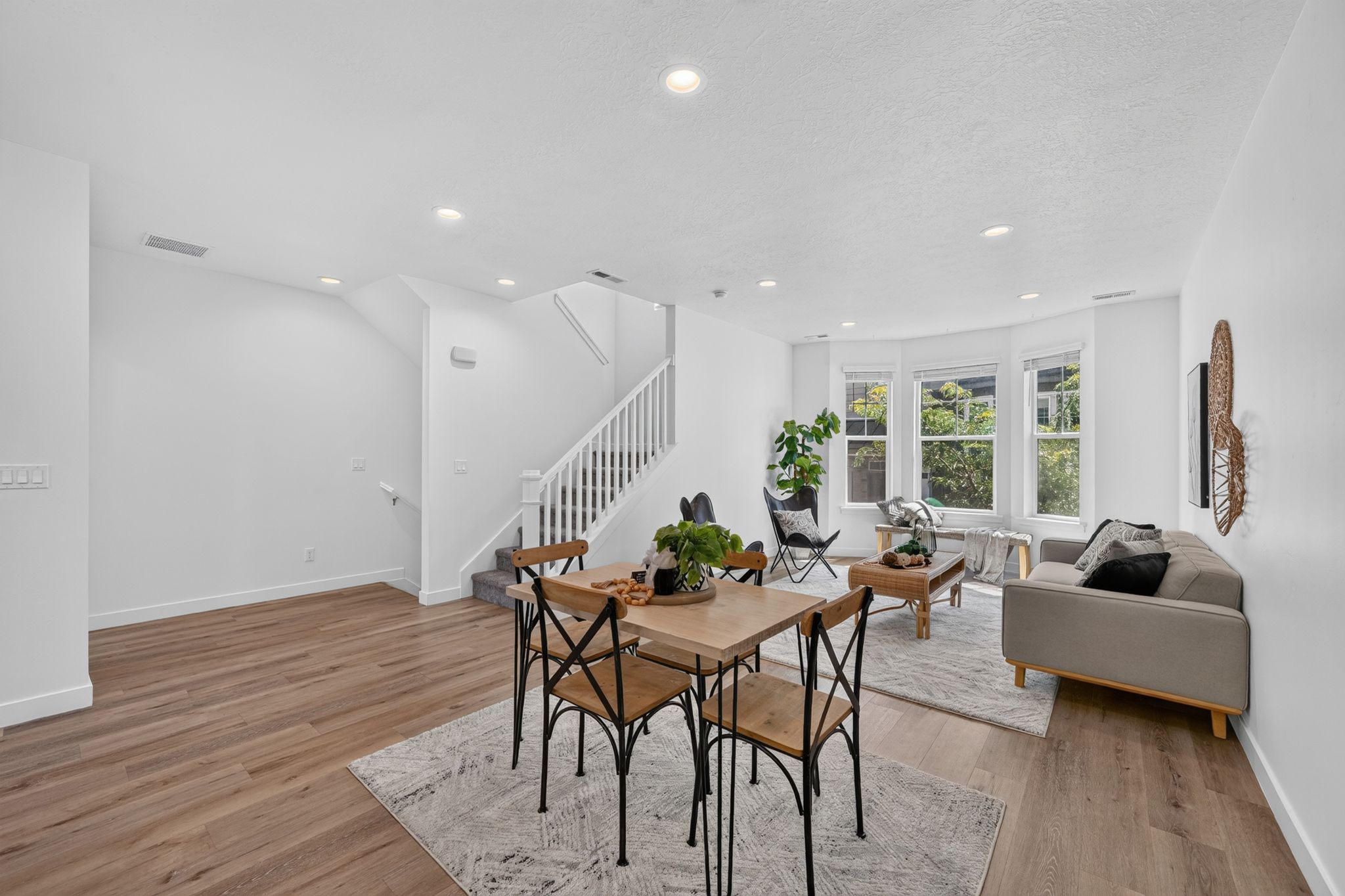 Open-concept living space featuring wood-finish flooring, recessed lighting, and a prominent staircase with white balusters