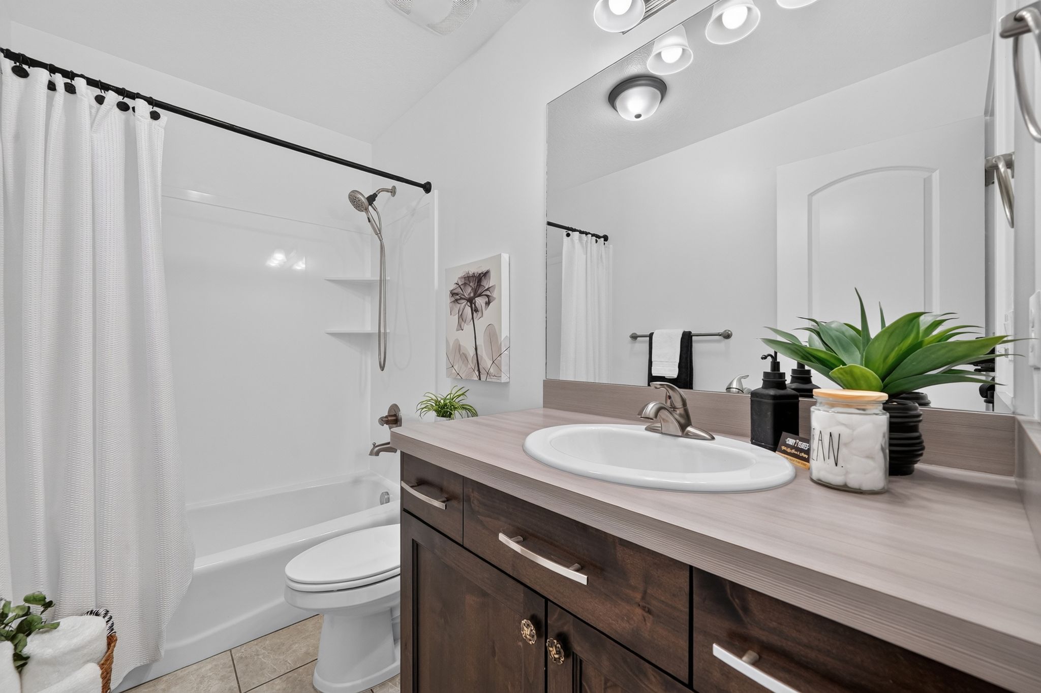 Bathroom featuring a white bathtub and shower combination with a curved shower curtain rod, a dark wood-finish vanity with a light countertop, an integrated sink, and a large mirror with overhead lighting