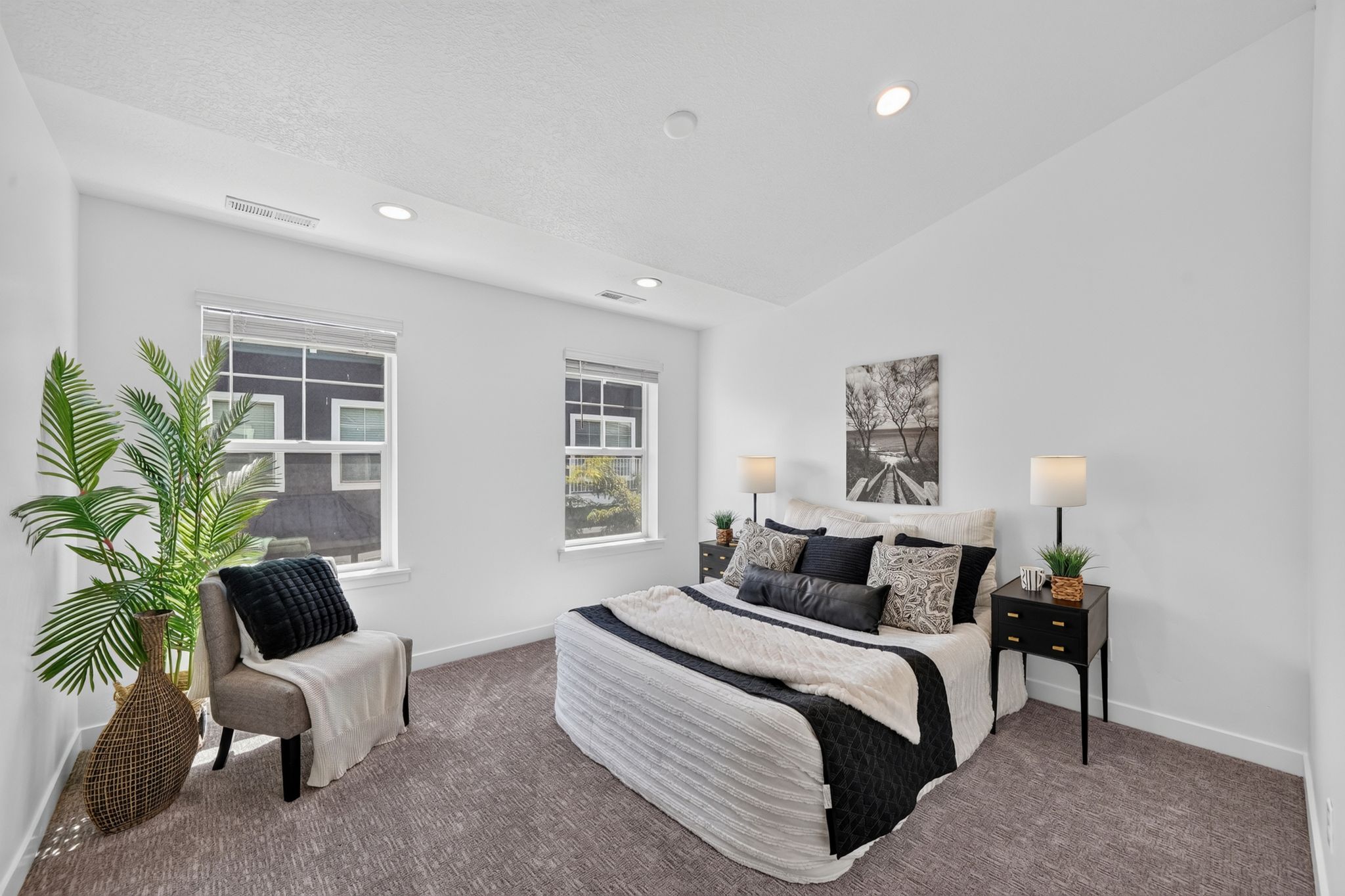 White walls provide a bright aesthetic in this room, featuring two windows with white blinds, recessed lighting, and grey patterned carpeting