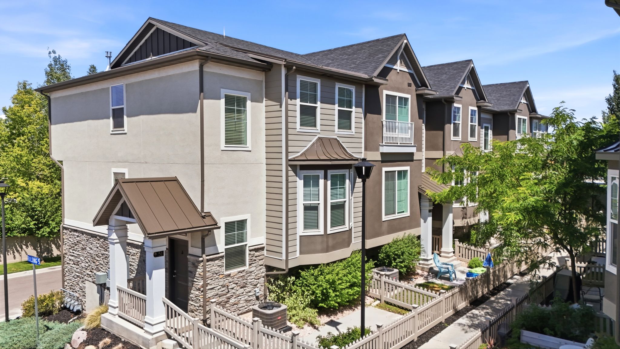 Contemporary townhome featuring a stone and stucco facade, a covered entry porch, and individual outdoor patios