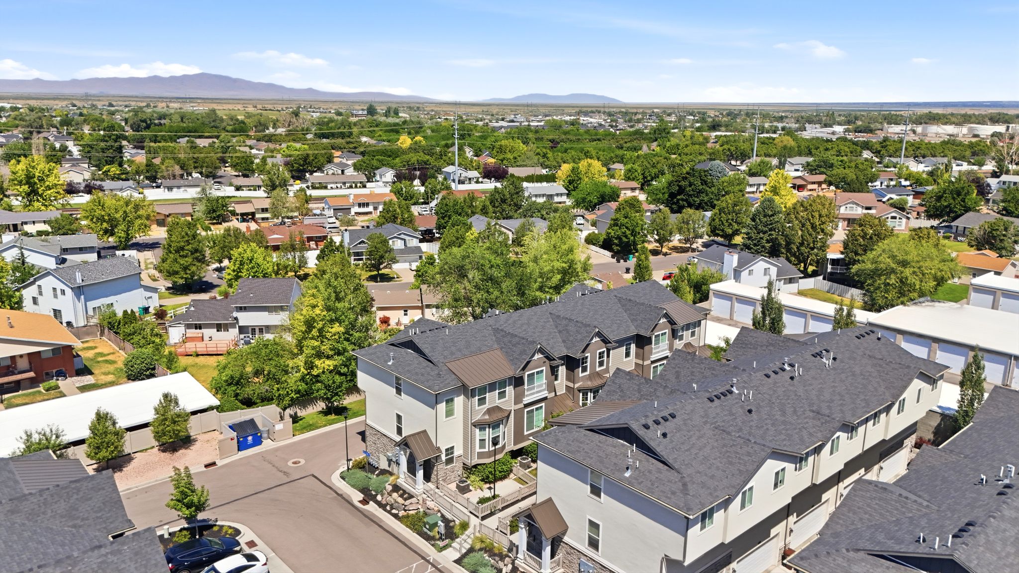 Modern townhome complex featuring multi-level units with dark shingle roofing, light-colored siding, and stone accents