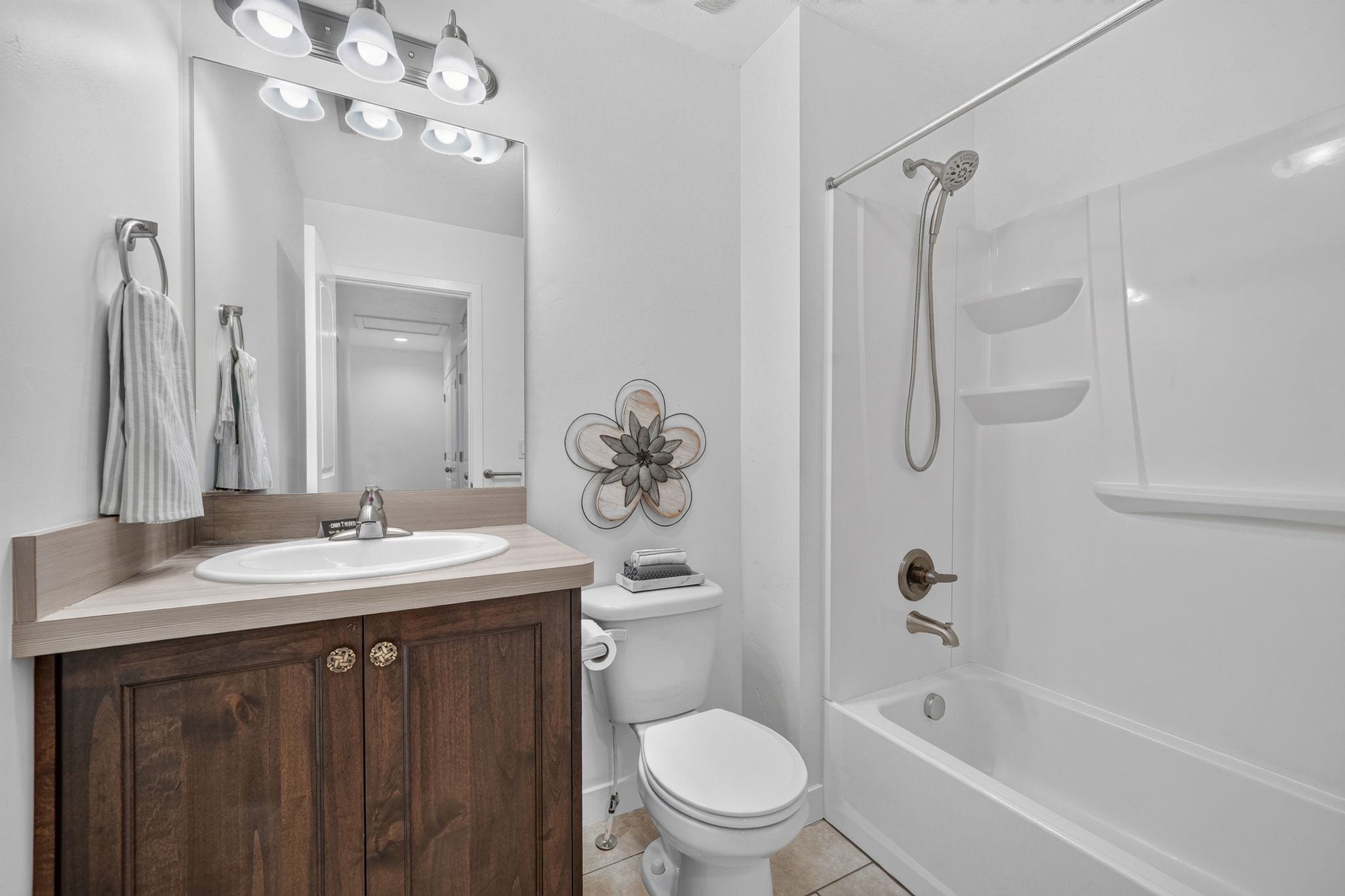 Full bathroom featuring a white tub and shower combination with bronze-finish fixtures, a single vanity with wood-finish cabinetry, a white oval sink, and a large mirror with overhead lighting