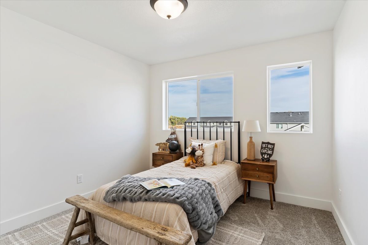 Bedroom featuring two distinct windows, a ceiling-mounted light fixture, white walls, and gray patterned carpet