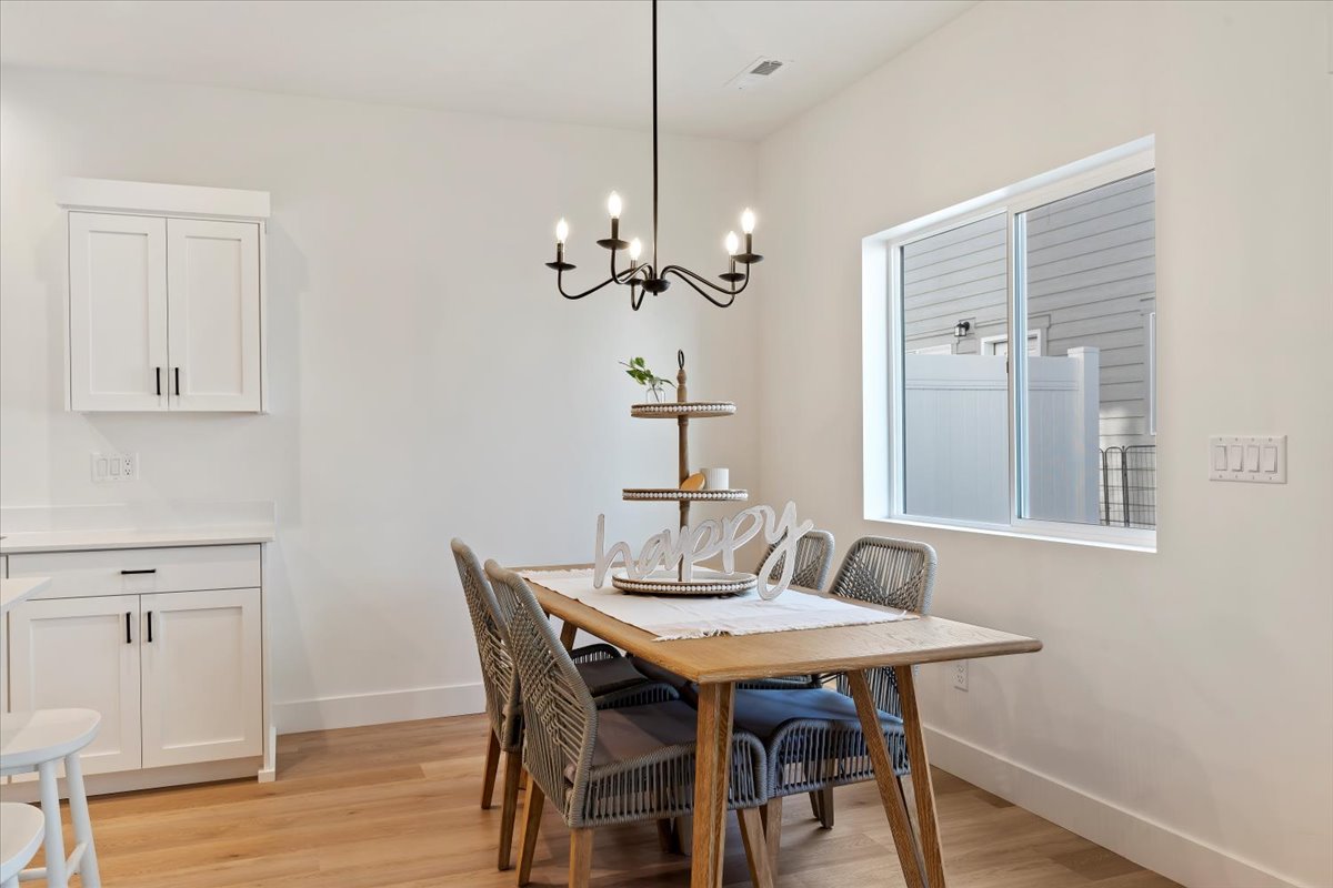 Dining area featuring wood-finish flooring, white walls, and a contemporary chandelier